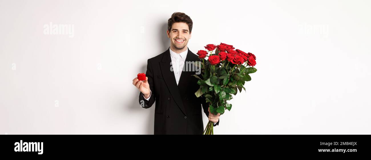 Image of handsome man in black suit, holding bouquet of red roses and a ...
