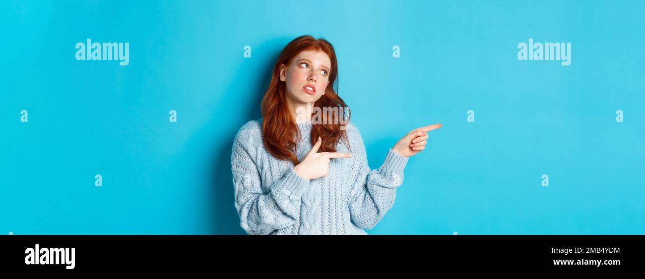 Annoyed teenage redhead girl roll eyes, pointing fingers left at