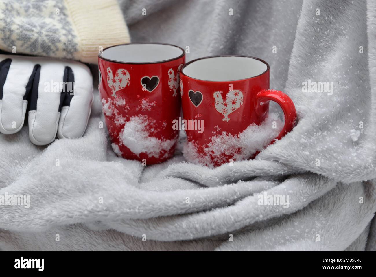 two red mugs with heart shaped on a plaid with snow and gloves and hat