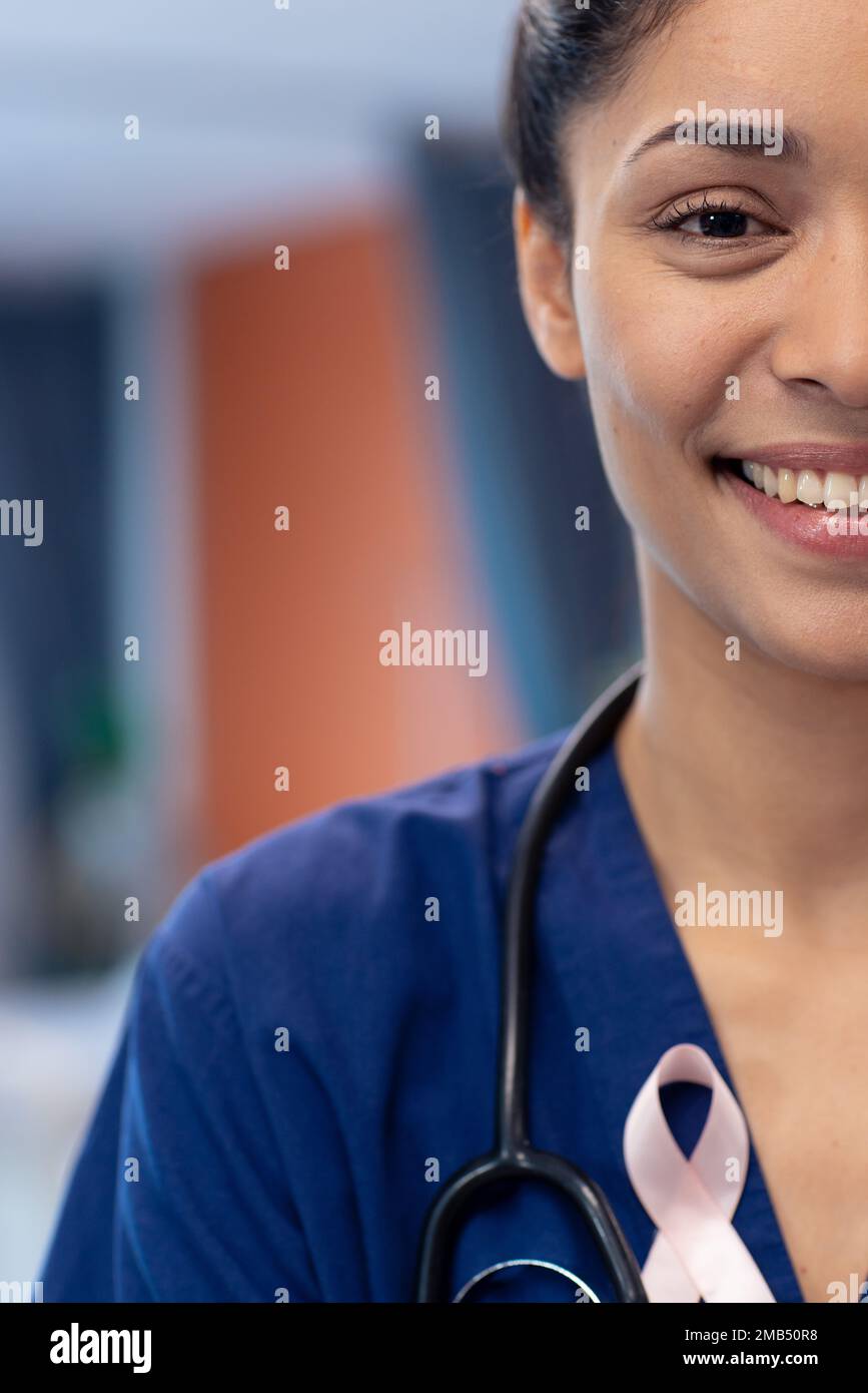 Vertical half face portrait of smiling biracial female doctor wearing cancer ribbon, copy space Stock Photo