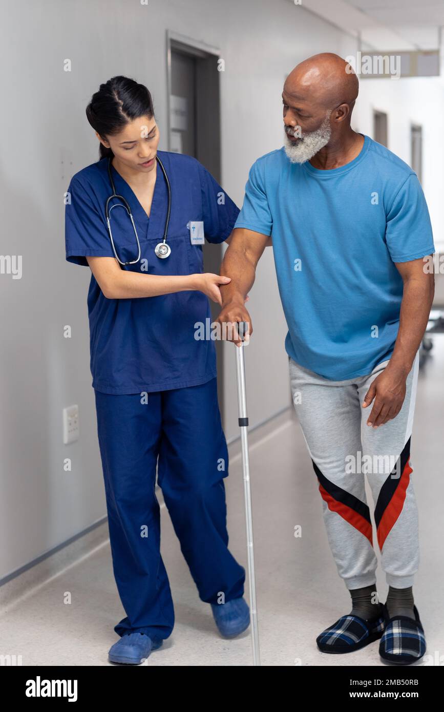 Vertical of diverse female doctor helping senior male patient use walking stick, copy space Stock Photo