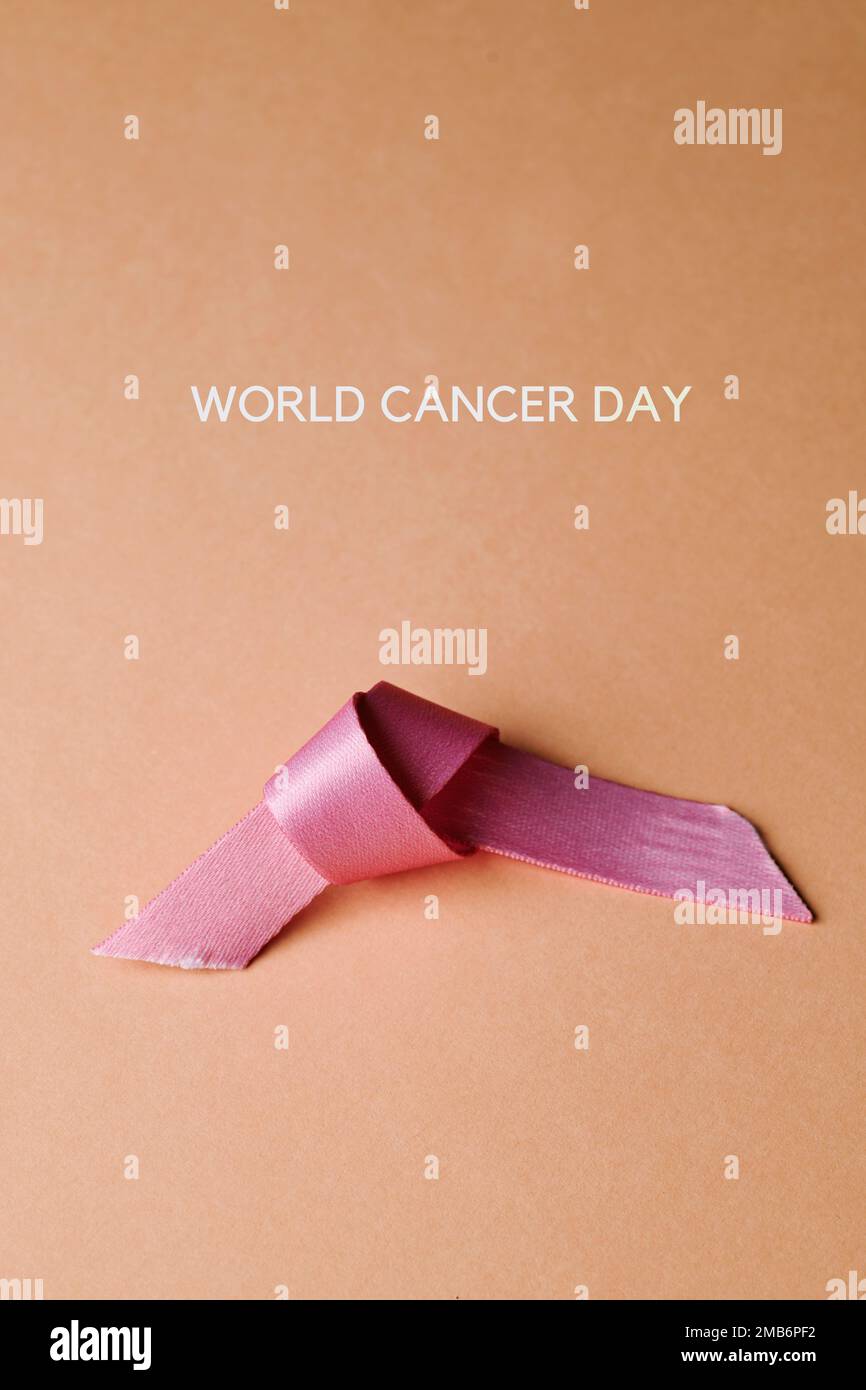 the text world cancer day and a used pink awareness ribbon on a pale pink background Stock Photo