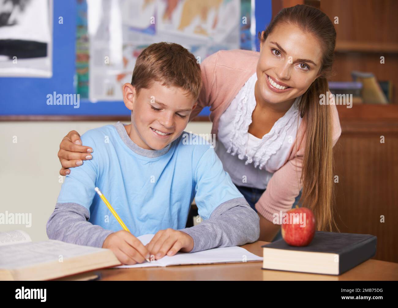 Just a bit of encouragement makes all the difference. A supportive young teacher leaning over her student while he writes in a book - portrait. Stock Photo