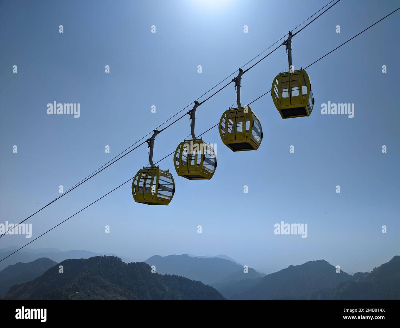 A low-angle of four yellow cable cars on the rope against a blue sky ...