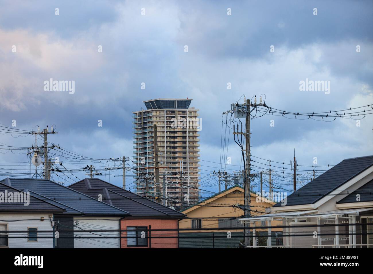 High rise apartment tower over electrical wires and suburban houses Stock Photo
