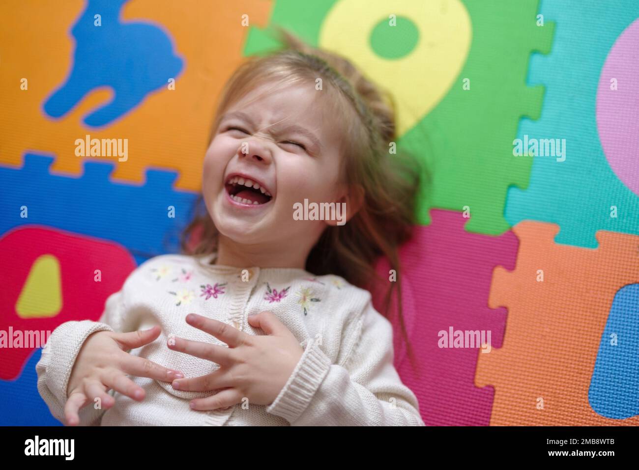 Happy Caucasian girl lying on puzzle mat Stock Photo - Alamy
