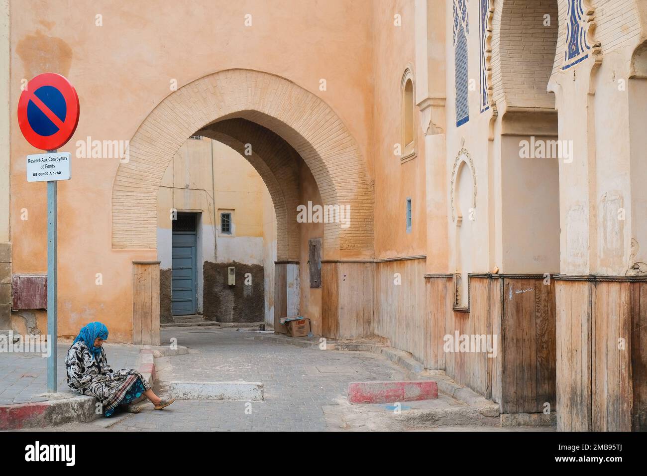 Fez, Morocco - original Bab Bou Jeloud gate in ancient Fes el Bali medina. Simple and modest medieval entrance. Old woman beggar sits on the curb. Stock Photo