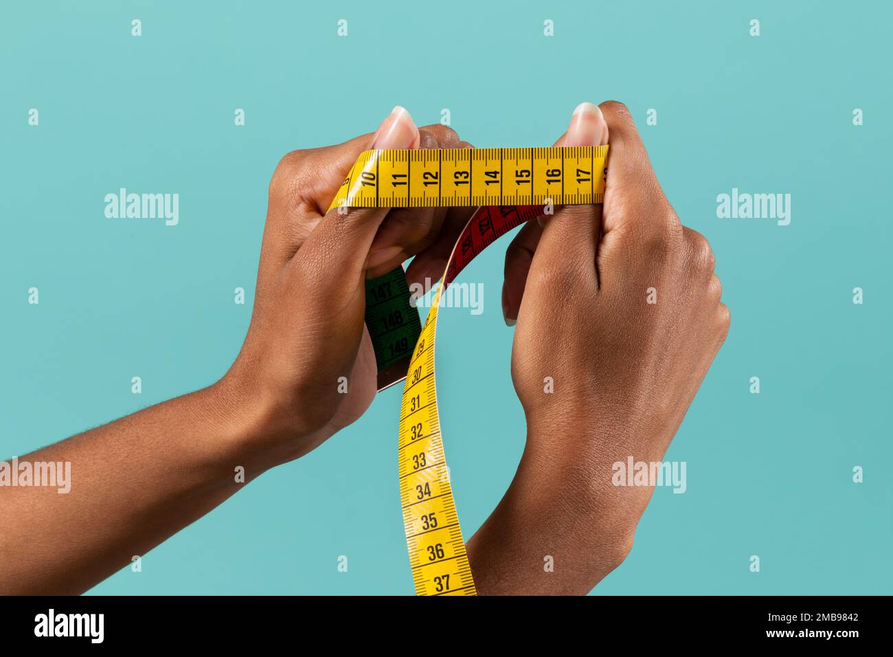 Crop anonymous African American female hands demonstrating yellow measuring tape on turquoise background Stock Photo