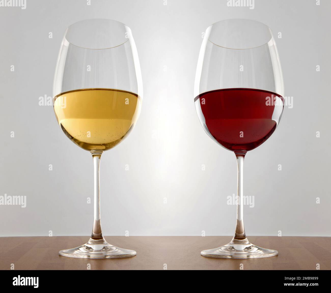 Glasses of white and red wine placed on wooden desk against gray background Stock Photo