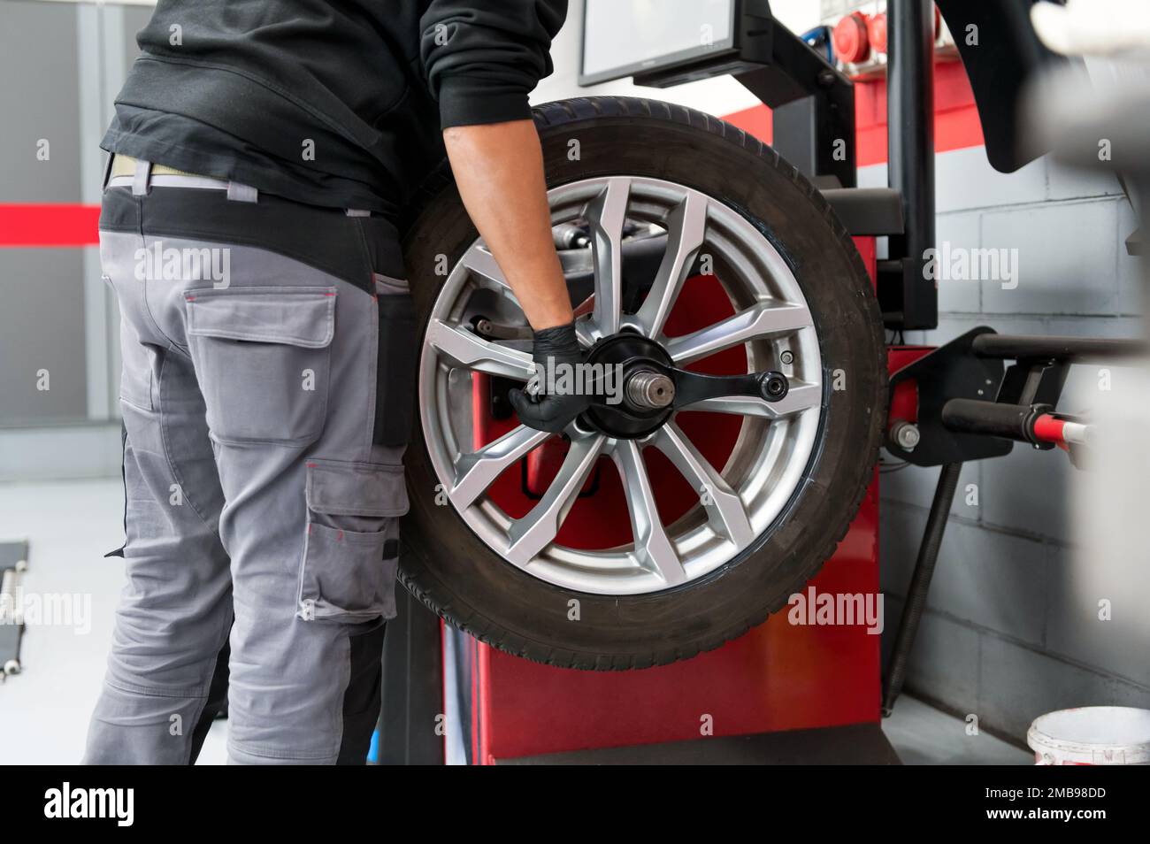 Side view of crop unrecognizable male mechanic in casual wear and gloves fixing car wheel during work in modern garage Stock Photo