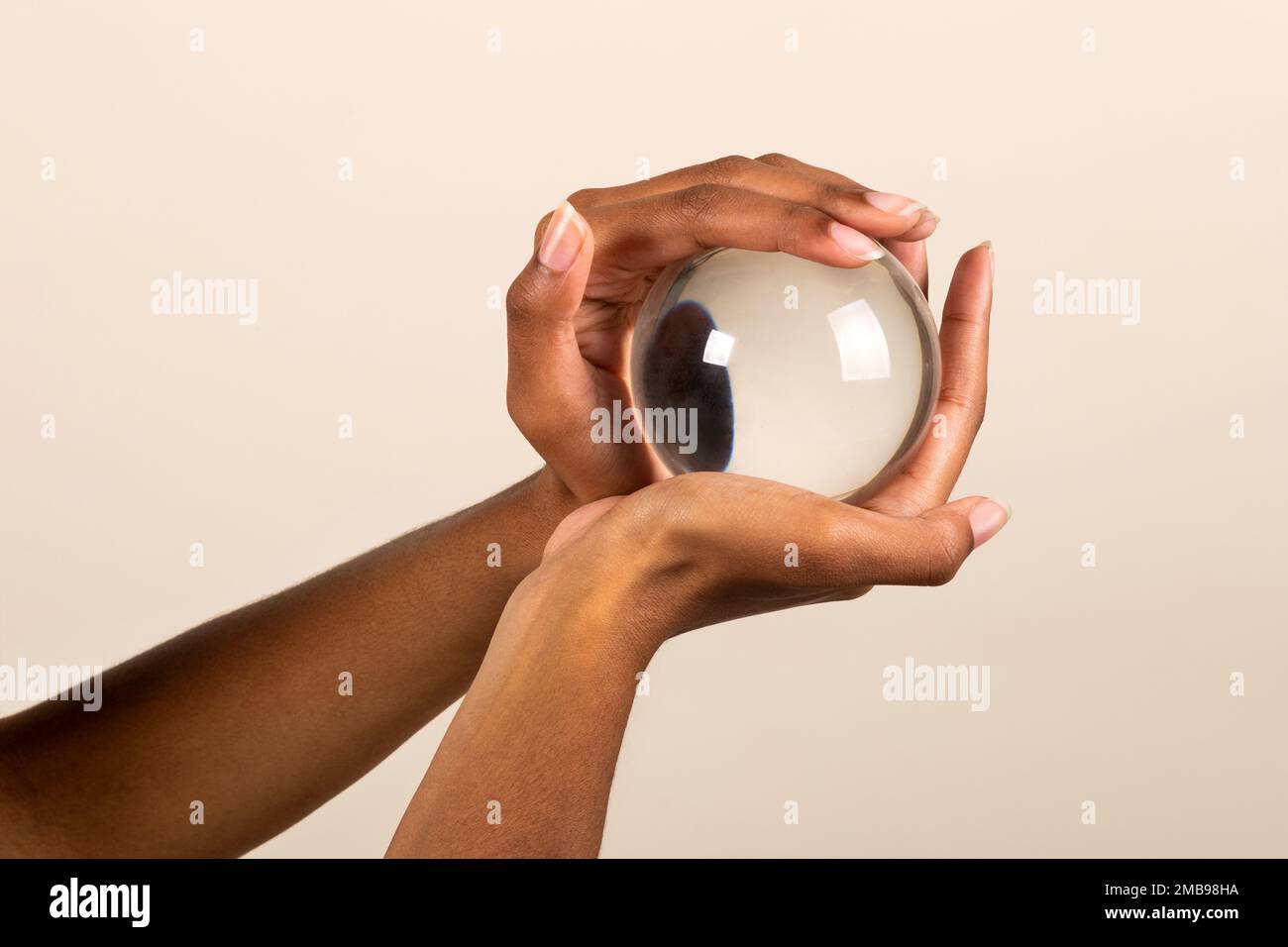 Closeup of crop anonymous African American female holding transparent glass sphere in hands on pink background Stock Photo