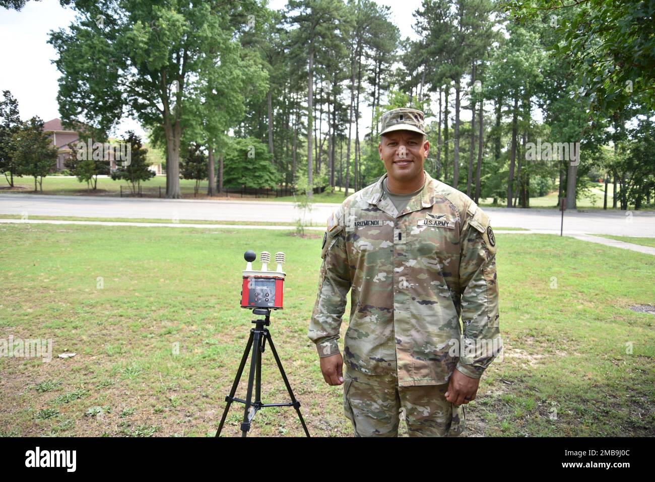 1st Lt. Ansel Arizmendi, chief of Environmental Health, Womack Army Medical Center (WAMC), stands beside the Wet Bulb Globe Temperature Monitor (WBGT) device used to monitor heating conditions outside of the Public Health building on Fort Bragg on June 13, 2022. Stock Photo