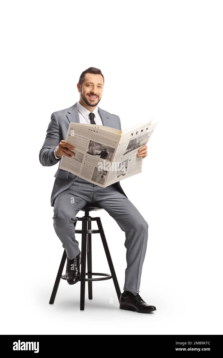 Young professional man in a suit sitting on a chair with a newspaper and smiling at camera isolated on white background Stock Photo