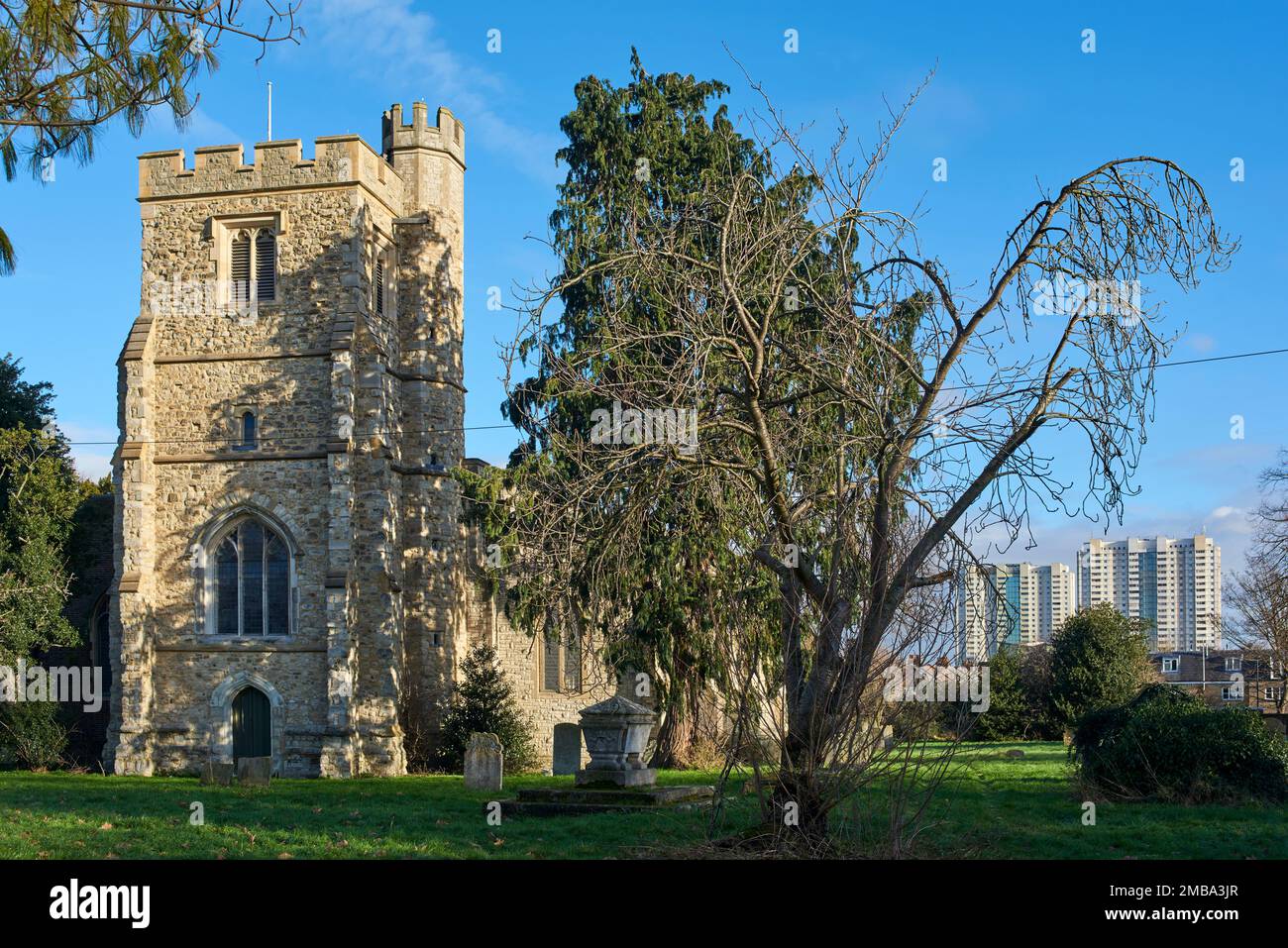 The tower and churchyard at All Saints church, Edmonton, North London, UK, with tower blocks in the background Stock Photo