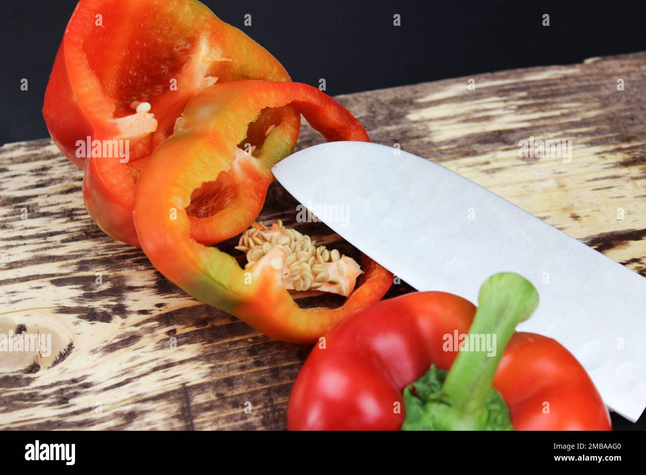 A pepper cut into two halves with a sharp knife. Knife lay next to cuttable pepper Stock Photo