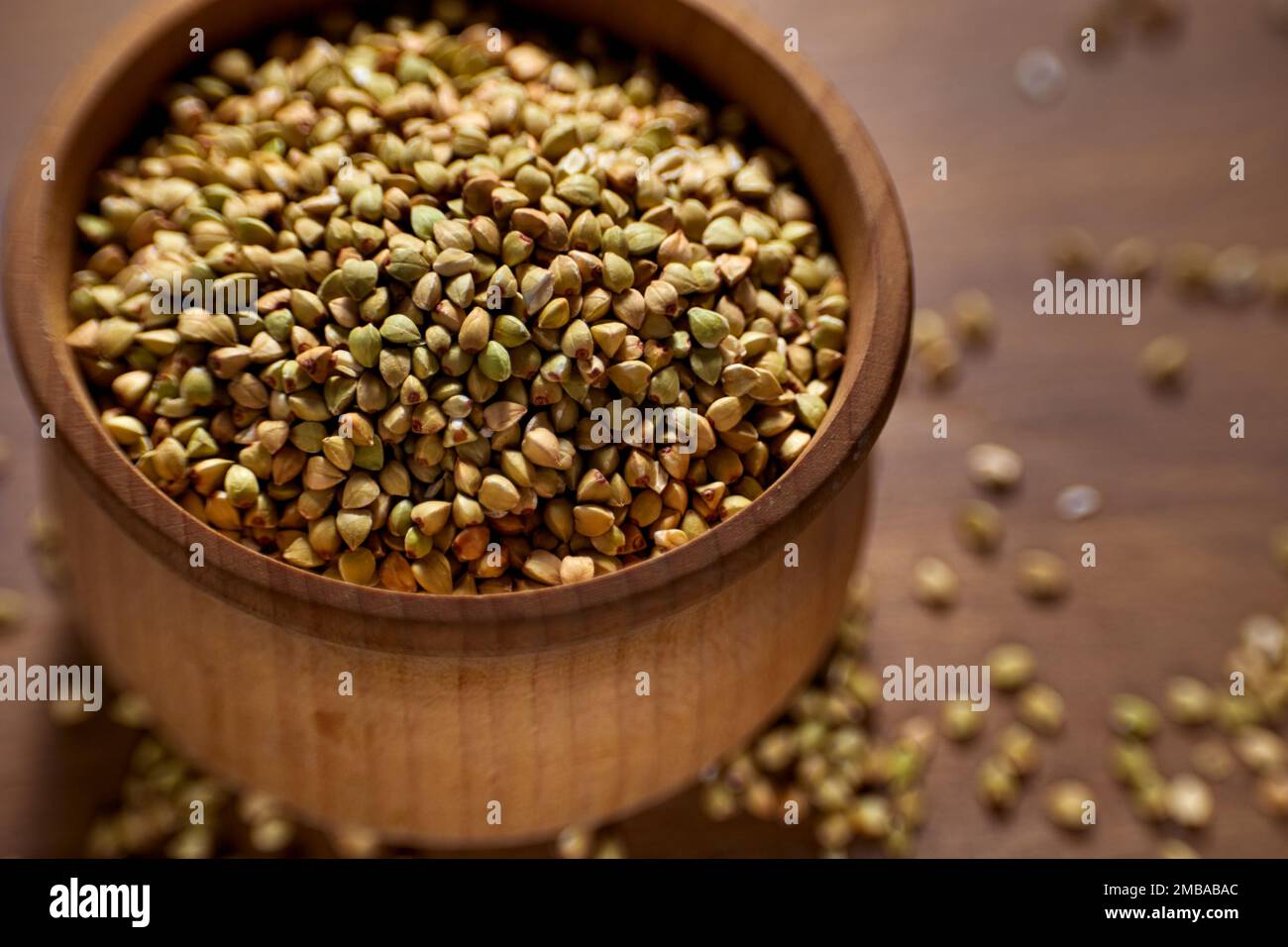 Unprocessed green buckwheat in a wooden bowl on a wooden board. Stock Photo