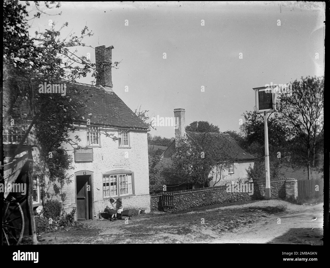 Beacon's Bottom, Stokenchurch, Wycombe, Buckinghamshire, 1919. A beer house and inn sign at Beacon's Bottom with two young girls sitting outside. At the time the photograph was taken Henry Butler was registered as a beer retailer in Beacon's Bottom. His name can just be seen on the sign above the door. Stock Photo