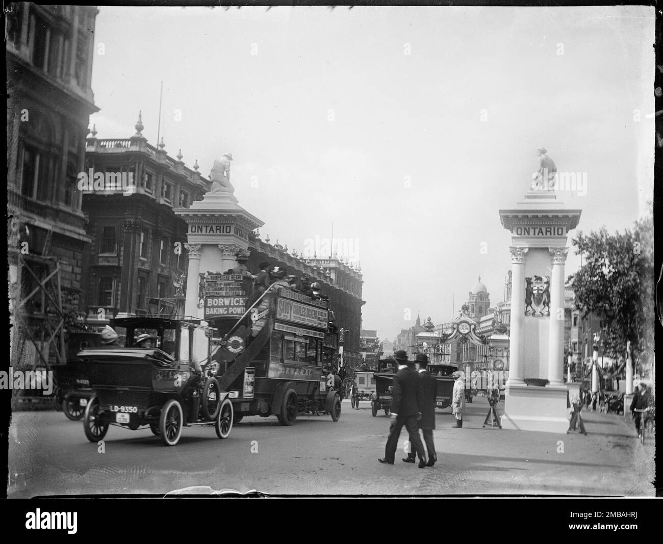Whitehall, City of Westminster, Greater London Authority, 1911. A view of a pair of columns surmounted by statues outside the Cabinet Office and Treasury on Whitehall, with traffic and pedestrians in the road. Taken to show coronation decorations in London. The photographer refers to the columns as 'Ontario Pillars' probably due to 'Ontario' appearing at the the top of the columns, but postcards of the time refer to them as 'Canadian Column'. The columns were erected to celebrate the coronation of King George V and Queen Mary on 22nd June 1911. Stock Photo