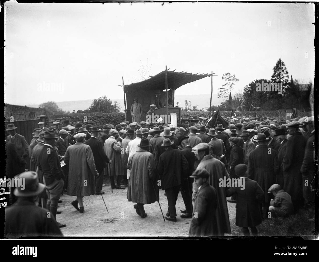 Stow-on-the-Wold, Cotswold, Gloucestershire, 1928. Looking over a crowd of men towards an auctioneers rostrum at the Stow Horse Fair, with a dark horse at the centre of the crowd. The auctioneers on the rostrum are from Cotswold auctioneers and valuers Tayler &amp; Fletcher. Stock Photo