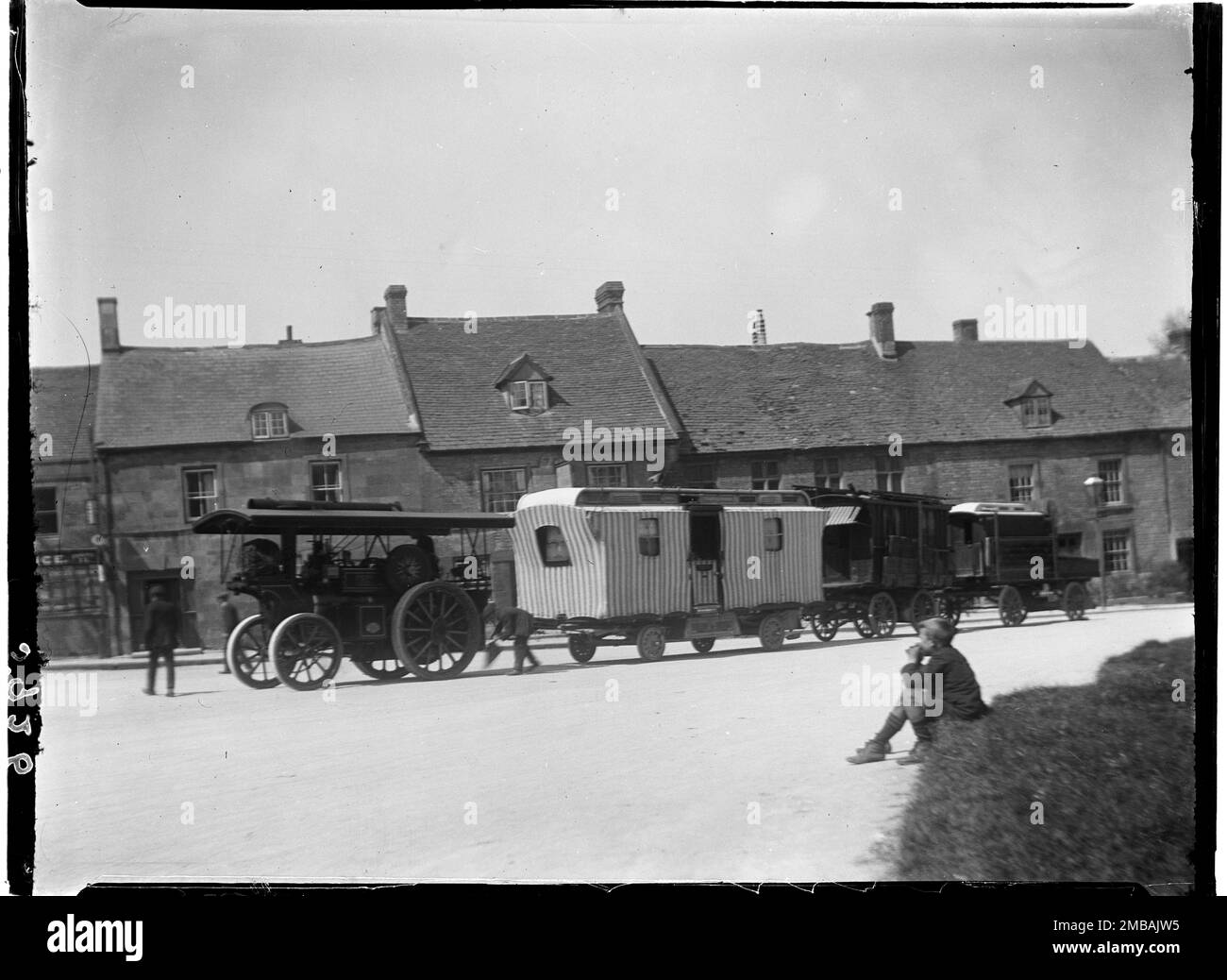 Stow-on-the-Wold, Cotswold, Gloucestershire, 1928. A steam-powered vehicle pulling gypsy caravans to the Stow Horse Fair past a row of houses, with a young boy watching from the foreground. Stock Photo