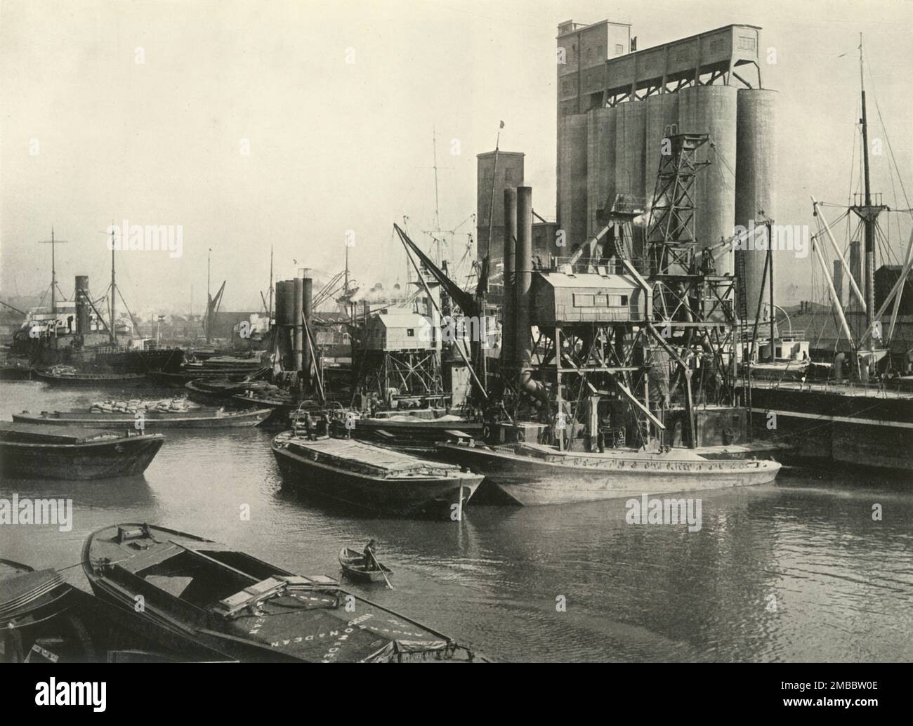 &quot;Factories, Refineries, Granaries Grow Thick&quot; Ship Discharging Grain by Floating Pneumatic Elevators and Into Quayside Mill at Millwall Dock', 1937. Industrial scene on the River Thames in London. From &quot;The Said Noble River&quot;, by Alan Bell. [The Port of London Authority, London, 1937] Stock Photo