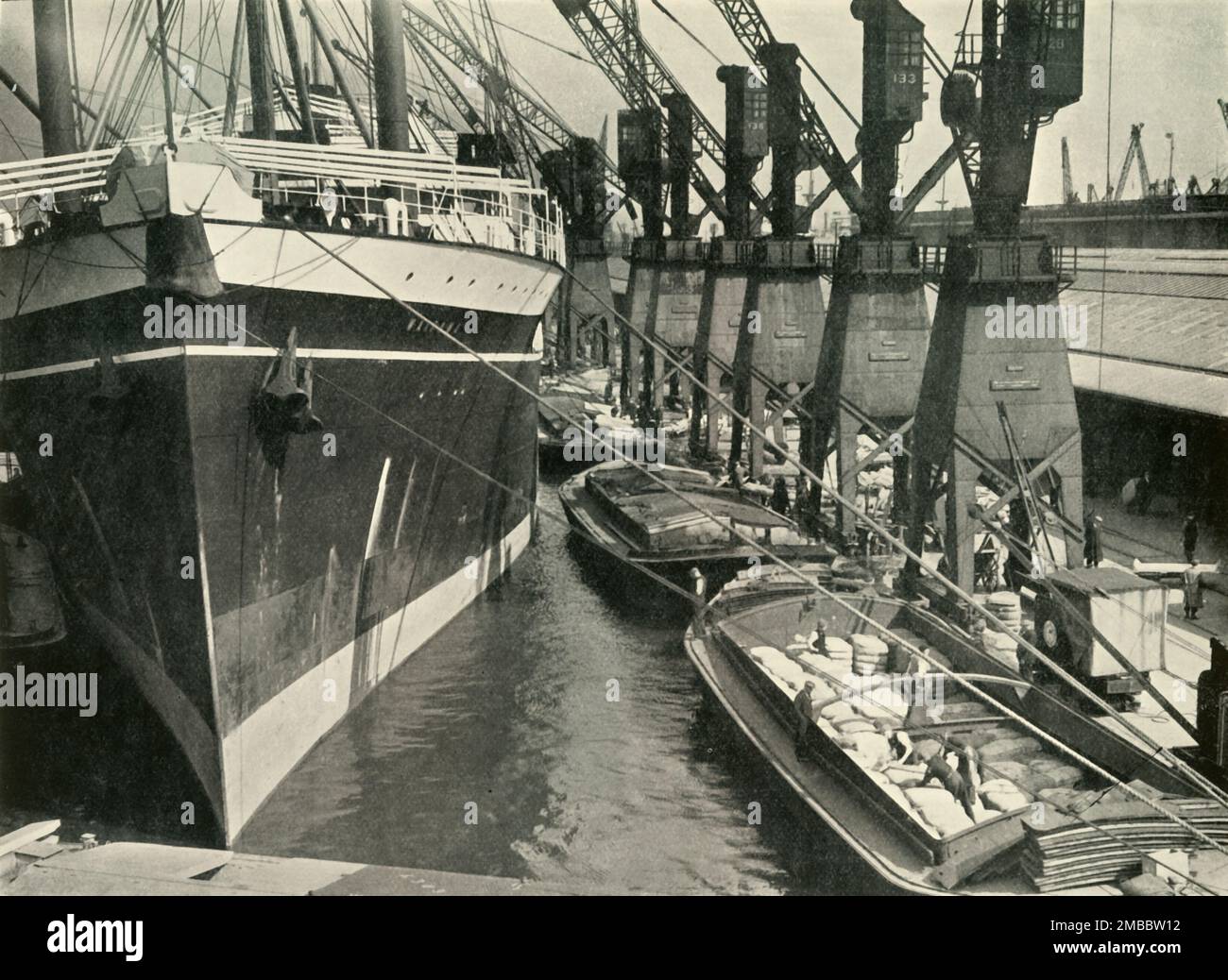 &quot;Goods of Whatever Sort Find Here the Appropriate Facilities for Unloading, Storage and Distribution&quot; South Quay, Royal Albert Dock, 1937. Cranes on the River Thames in London. From &quot;The Said Noble River&quot;, by Alan Bell. [The Port of London Authority, London, 1937] Stock Photo