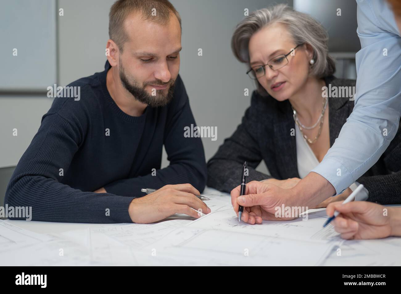 Four colleagues are discussing blueprints in a conference room in an office. Brainstorming of engineers and architects. Stock Photo