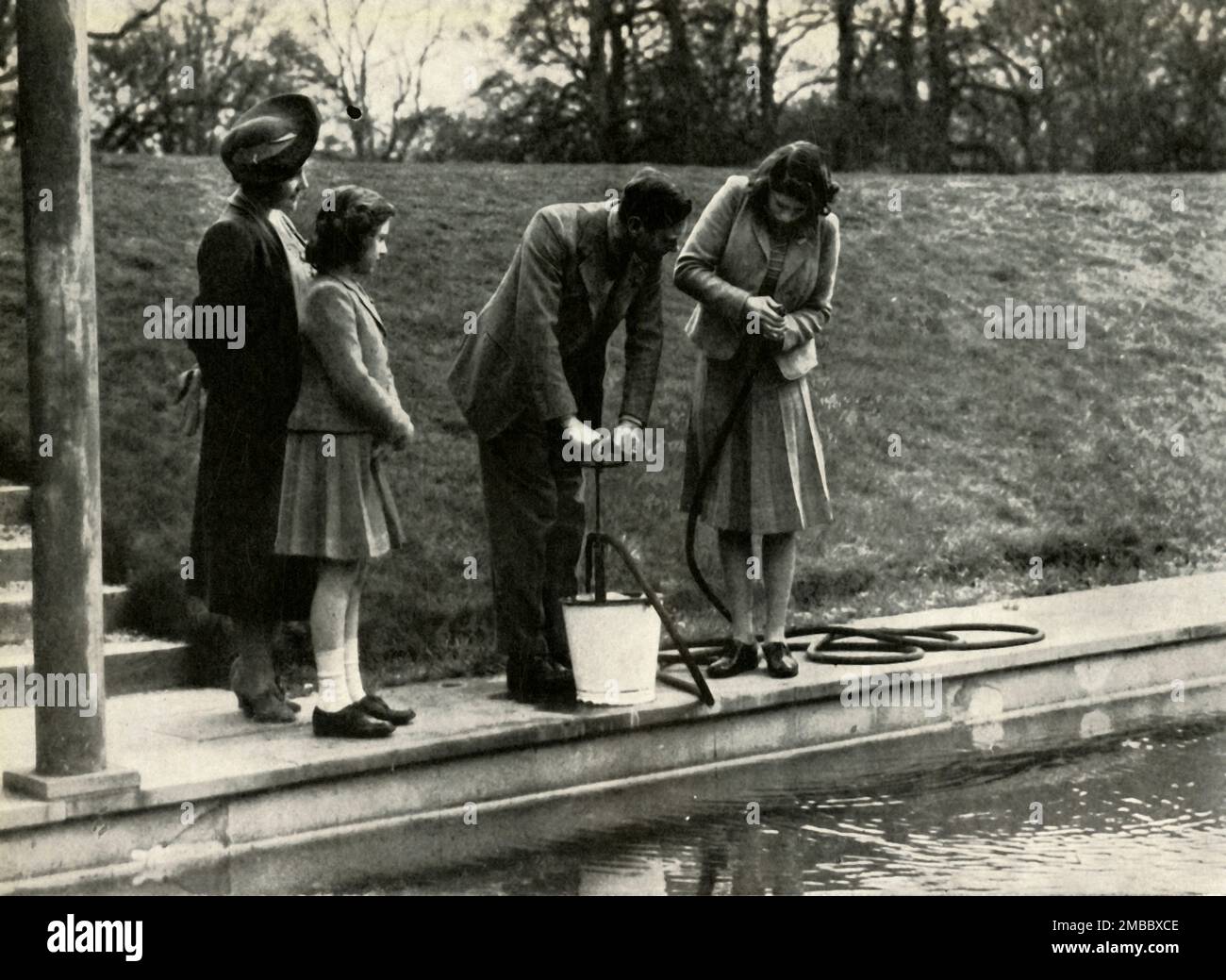 'Wartime at Windsor', 1941, (1947). King George VI and Queen Elizabeth with daughters Princess Elizabeth (future Queen Elizabeth II) and Princess Margaret Rose. In 1940 the princesses went to live at Windsor for the duration of the Second World War. Here we see the King and Princess Elizabeth at stirrup pump practice. From &quot;Princess Elizabeth: The Illustrated Story of Twenty-one Years in the Life of the Heir Presumptive&quot;, by Dermot Morrah. [Odhams Press Limited, London, 1947] Stock Photo