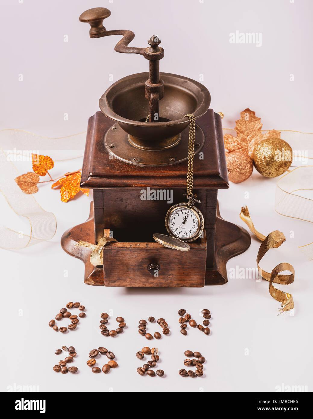 Coffee beans make up the inscription Buon 2023 which in Italian means happy 2023, with an antique wooden coffee grinder and a pocket watch in the back Stock Photo