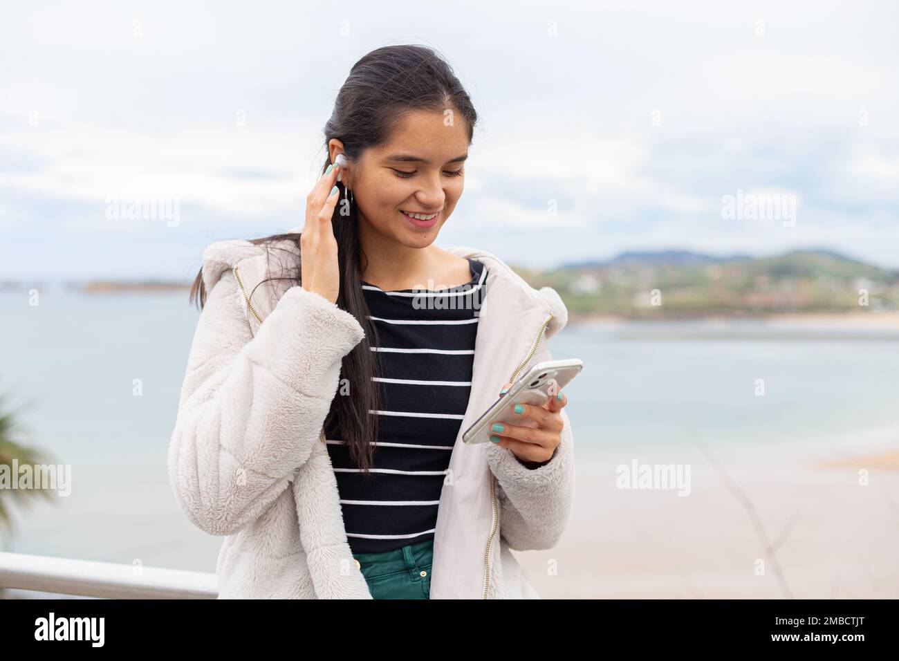Hispanic lady with smartphone listening to music in wireless earphones Stock Photo