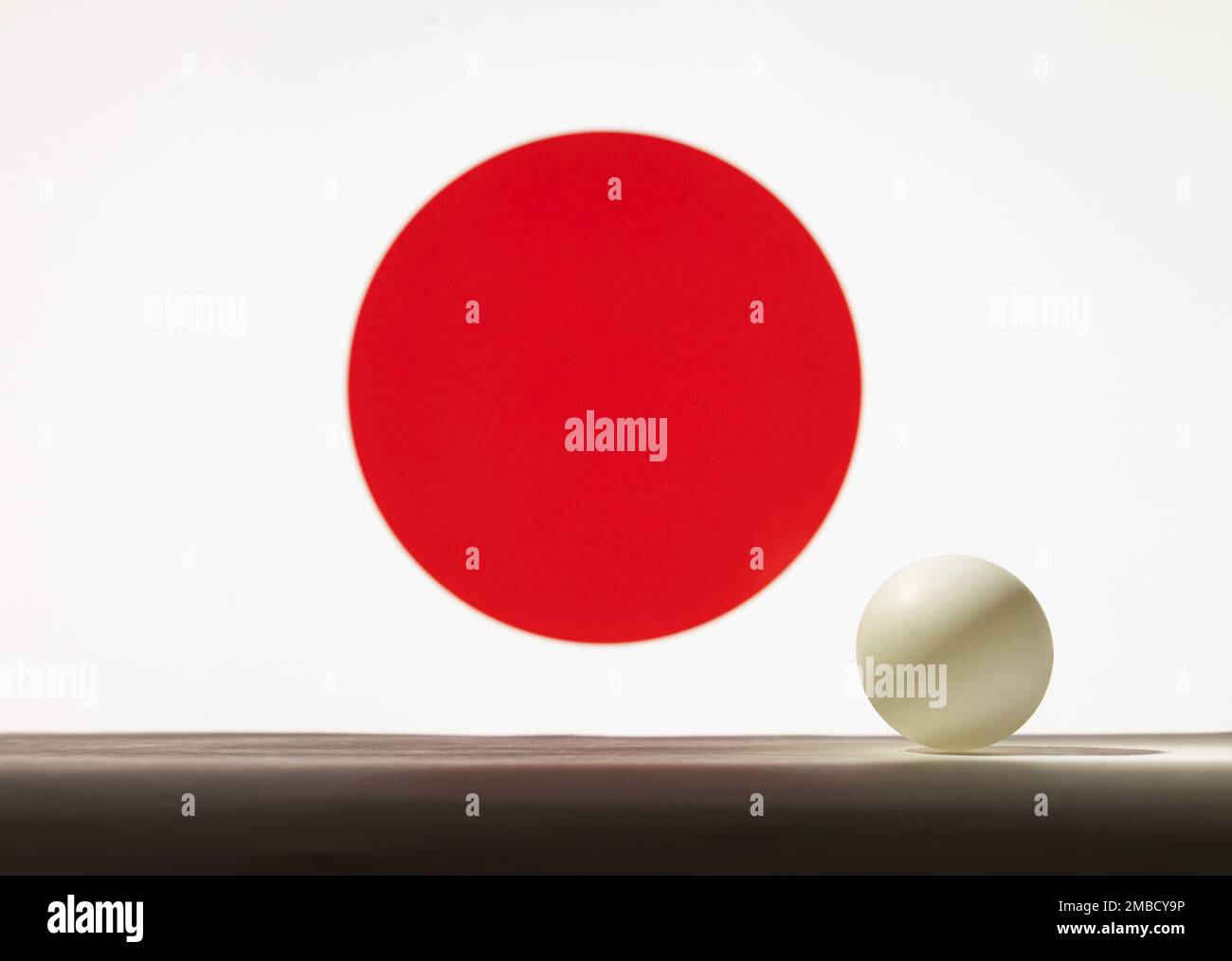 The Table tennis white ball stands on a surface in front of Japan flag