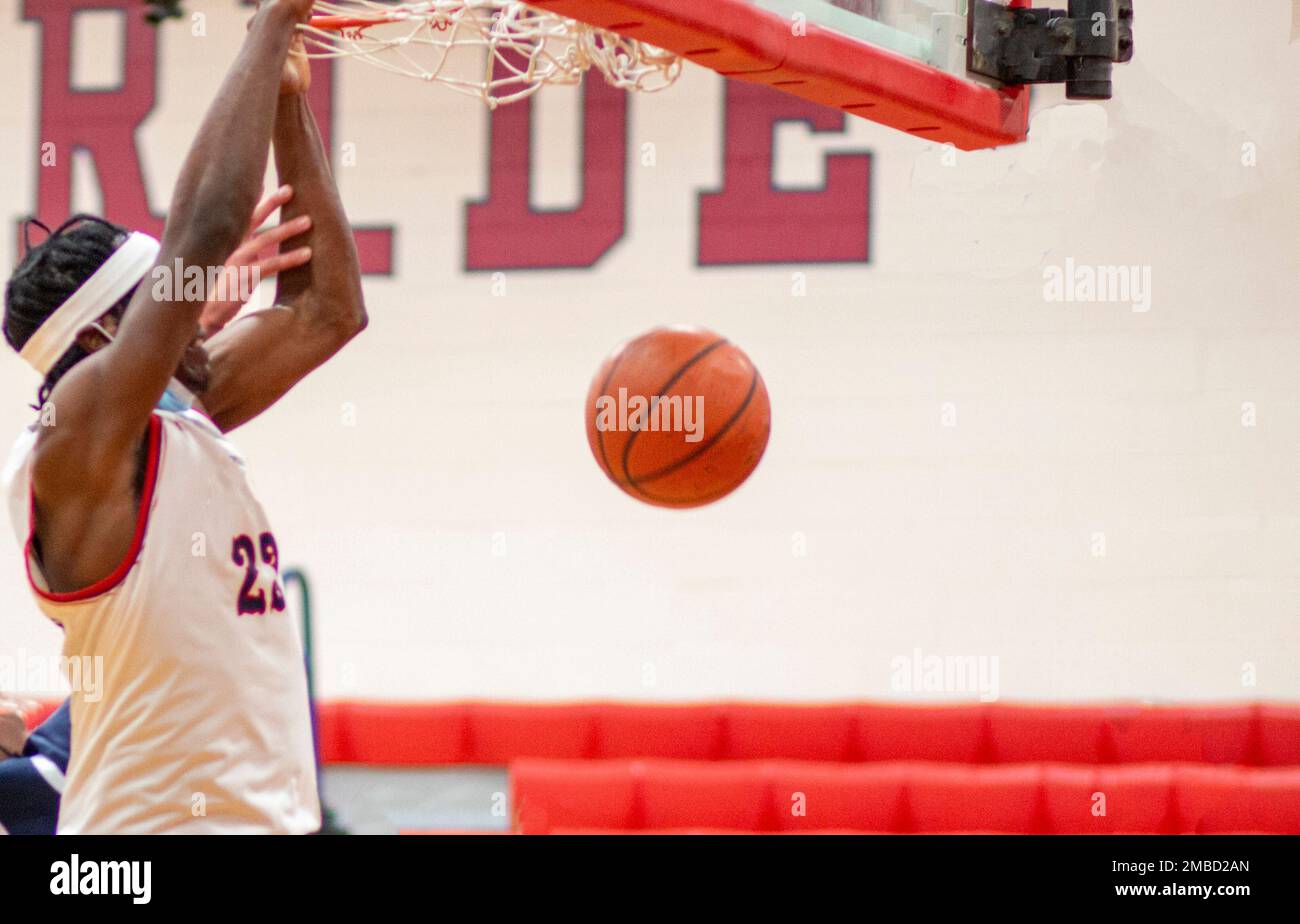 A high school basketball player hanging on the rim as the ball comes