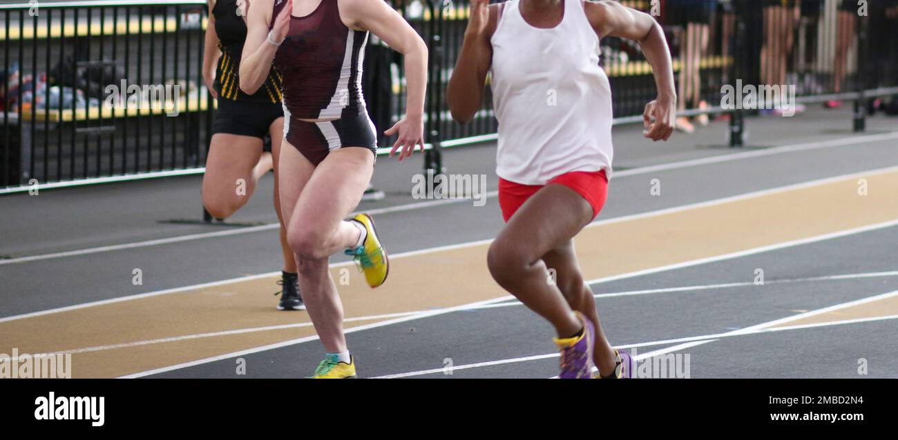 Three high school girls sprinting down an indoor track during an indoor