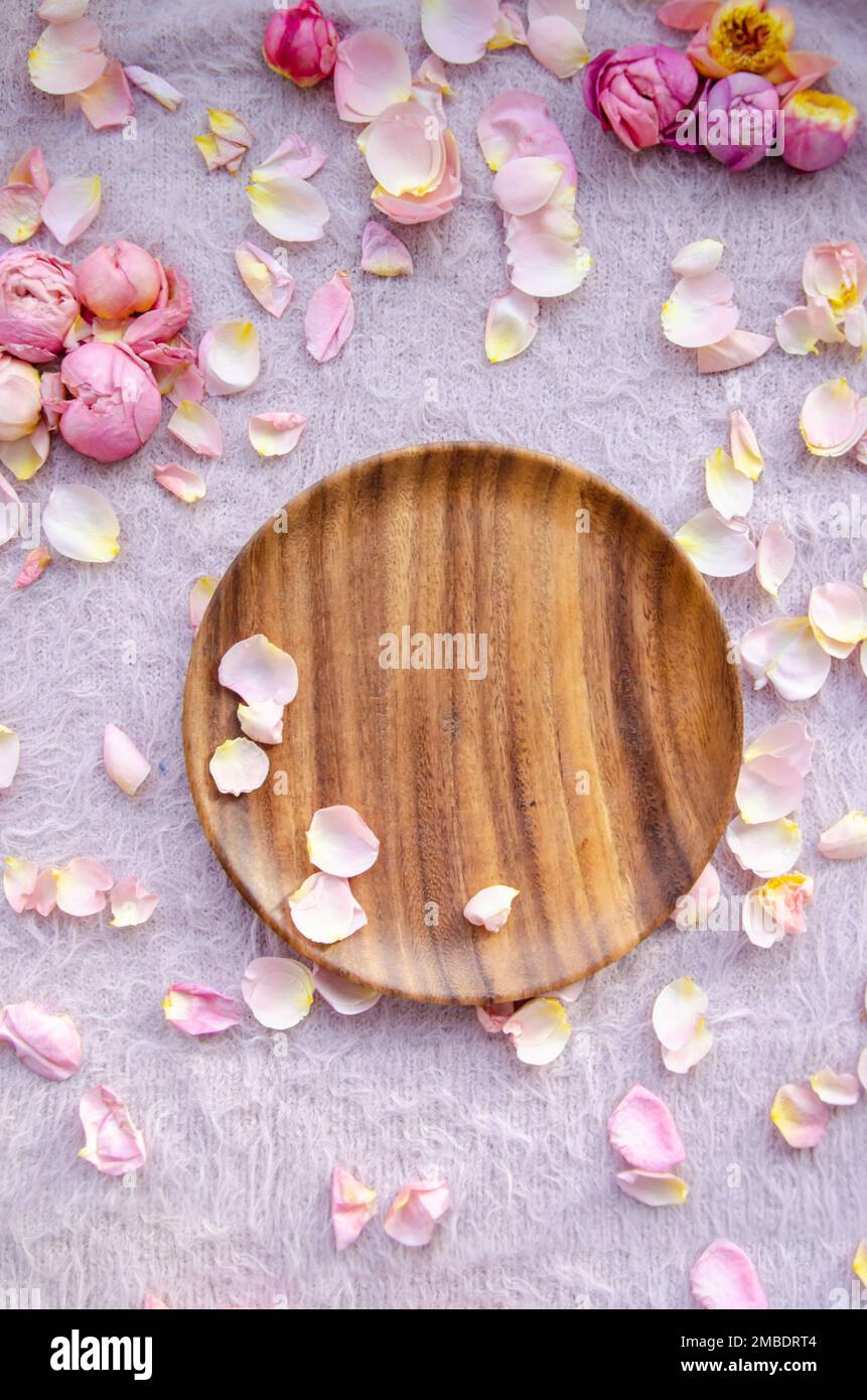Pink and yellow rose petals and rosebuds and wooden plate on knitted