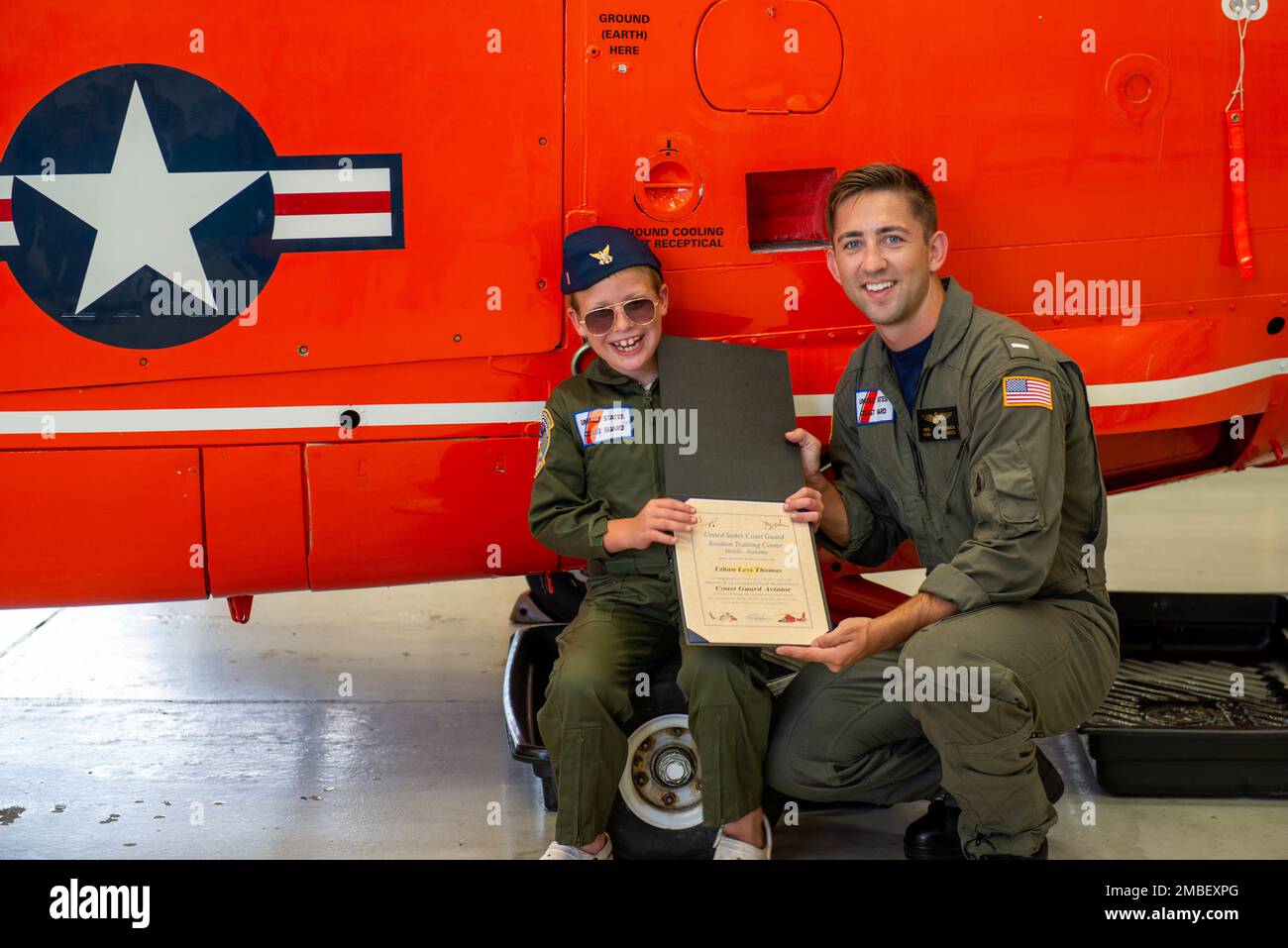 Coast Guard Lt. j.g. Nick Wittrock, pilot, and Ethan Thomas, an honorary aviator,  display his certificate at Coast Guard Aviation Training Center in Mobile, Alabama, June 15, 2022. Ethan was chosen to be part of ATC Mobile's Pilot-for-a-day program, which allows selected persons to visit the unit and have an in-depth tour of the aircraft and facilities. Stock Photo