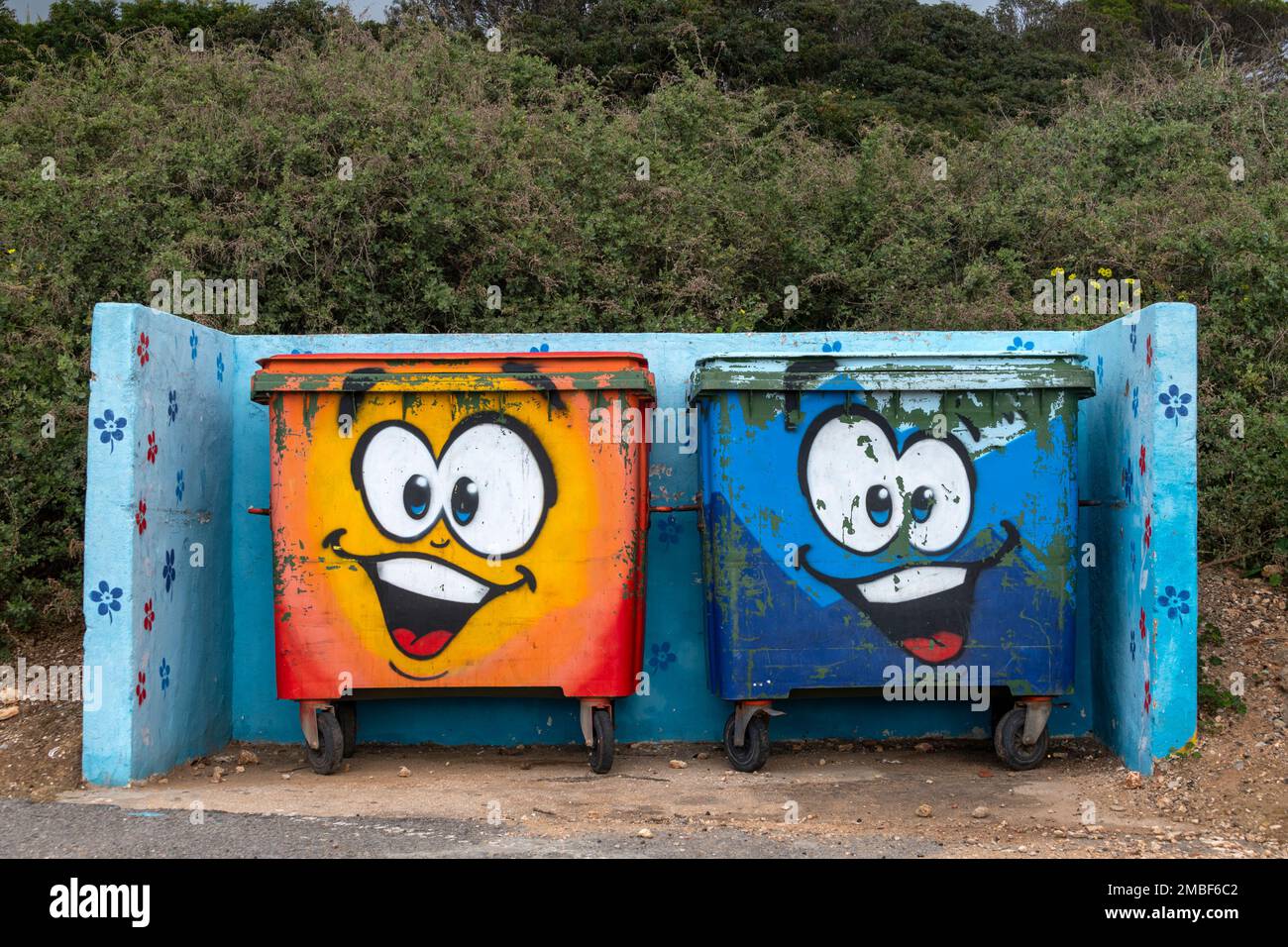 Two waste wheelie bins with graffiti cartoon faces painted on them