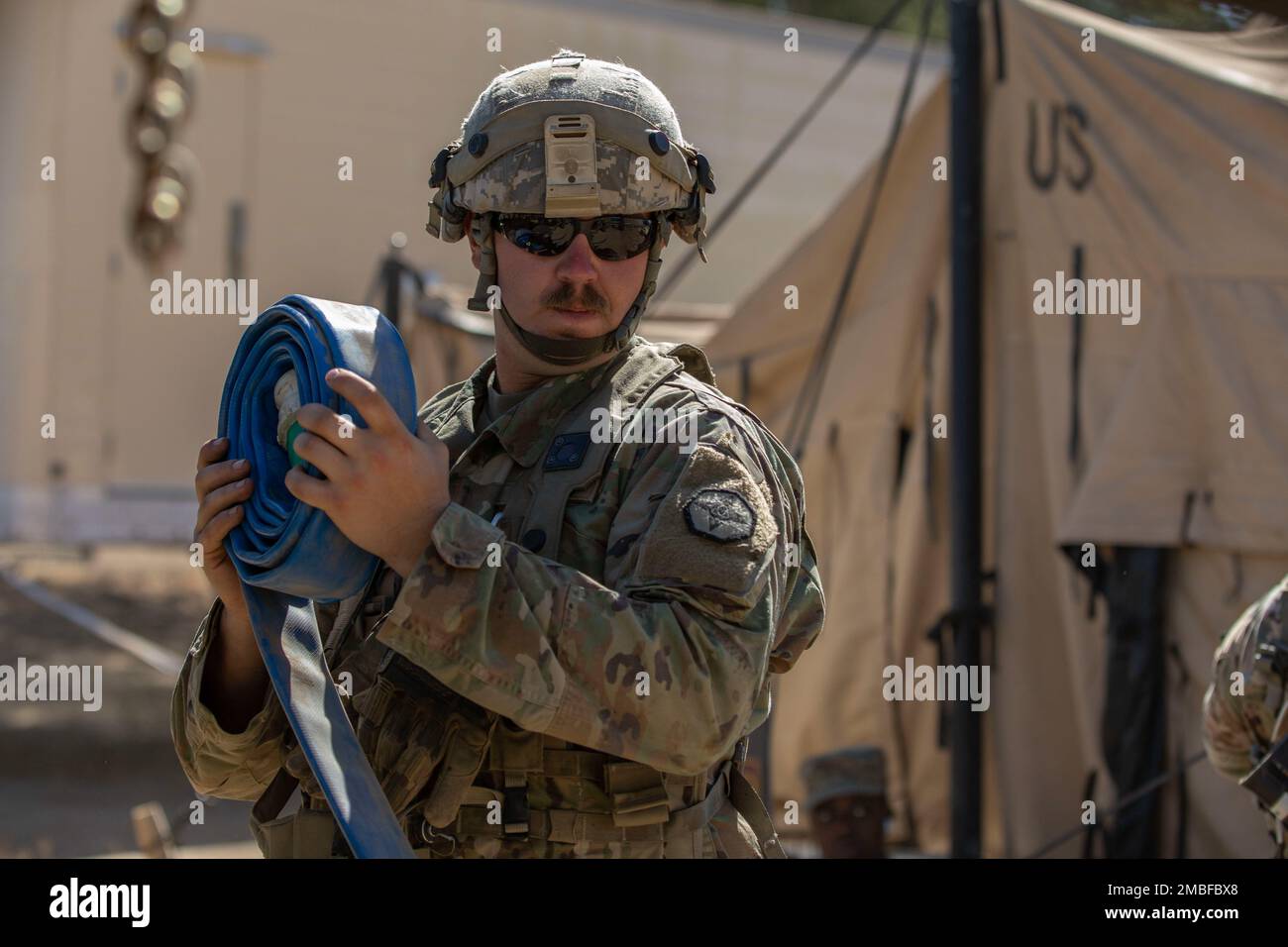U.S. Army Reserve Spc. Bryan Dakota, a water treatment specialist assigned to the 651st Quartermaster Company based in Casper, Wyoming, rolls up a hose used for transporting water from bags used for a shower tent during Combat Support Training Exercise 91-22-01 at Fort Hunter Liggett, California, June 15. Dakota has been a water treatment specialist in the Army Reserves for over six years and also works as a civilian crane operator. Stock Photo
