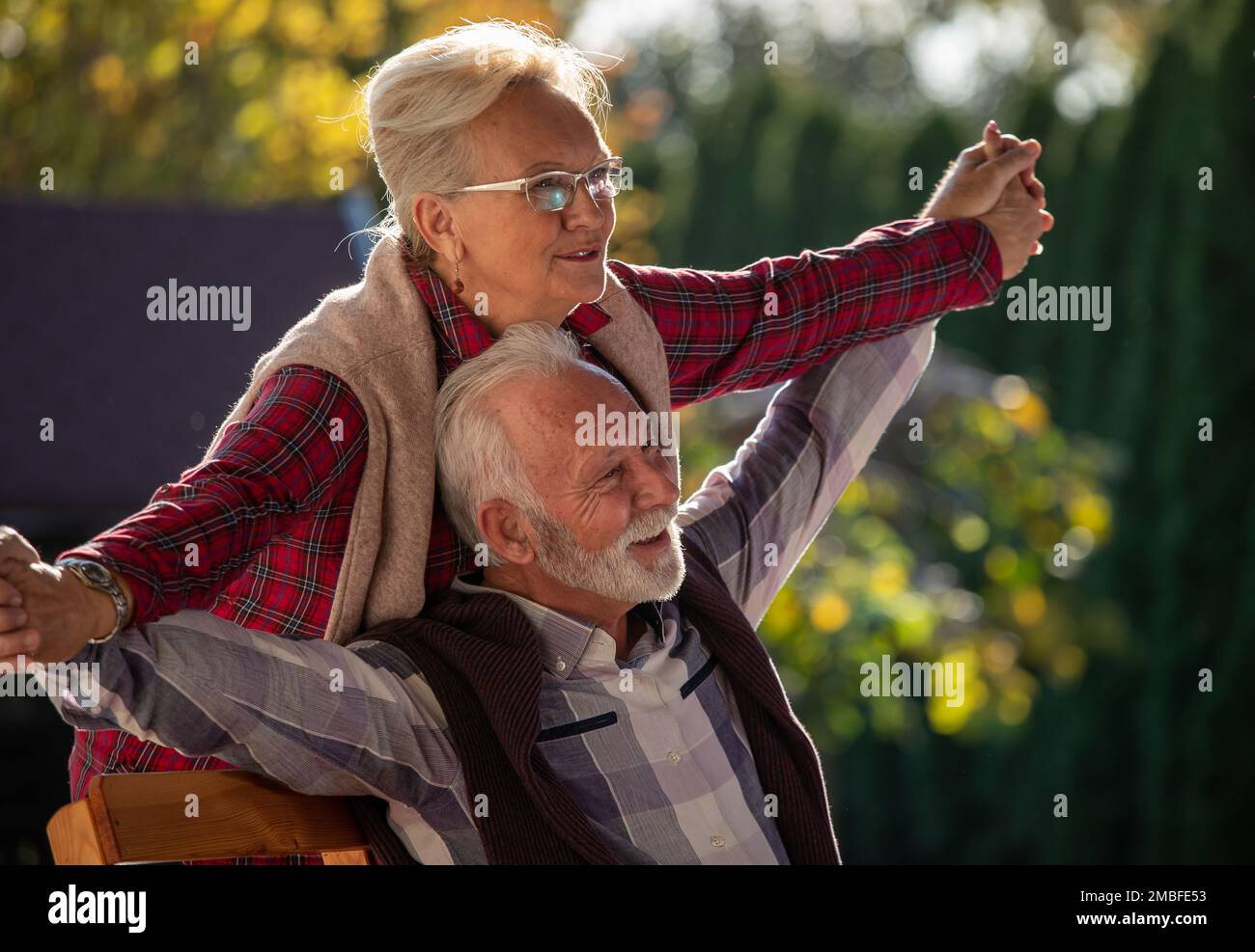 Senior woman holding spread hands of mature man behind him in park Stock Photo