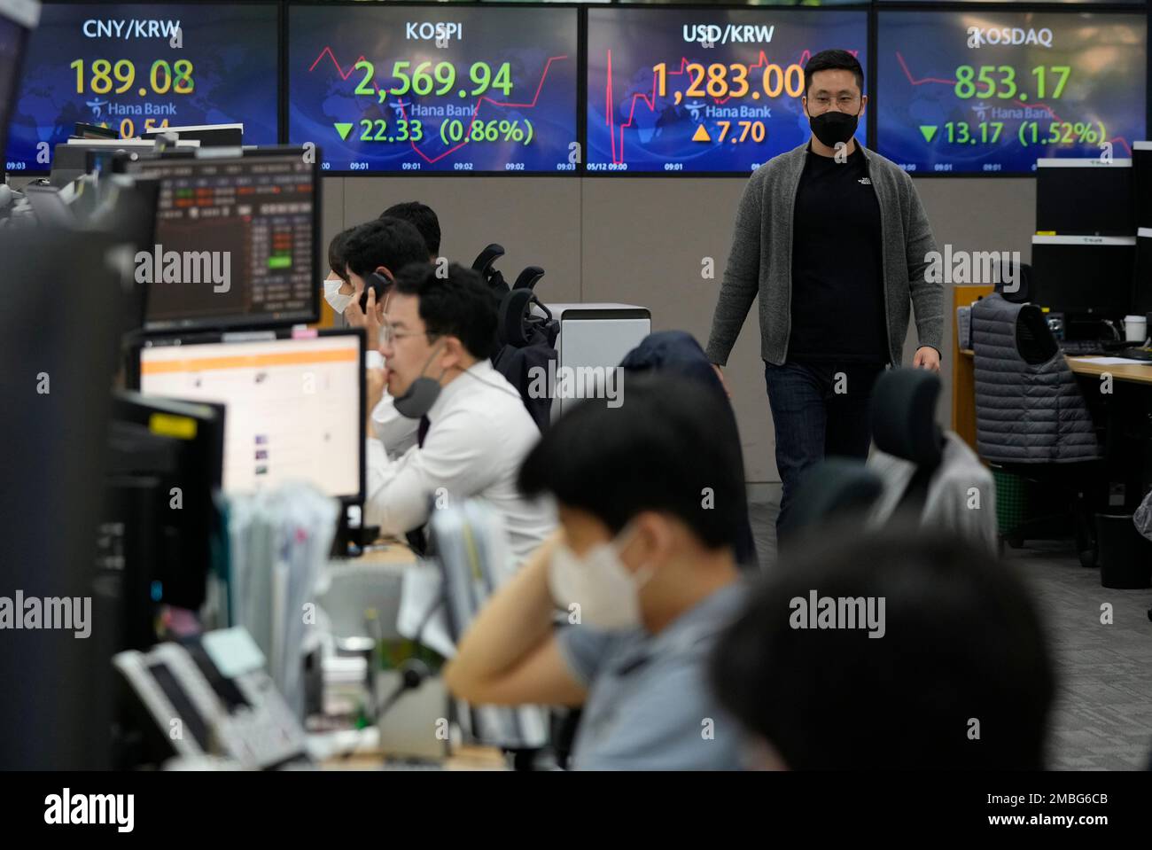 A currency trader passes by screens showing the Korea Composite Stock Price  Index (KOSPI), center left, and the exchange rate of South Korean won  against the U.S. dollar, center right, at the