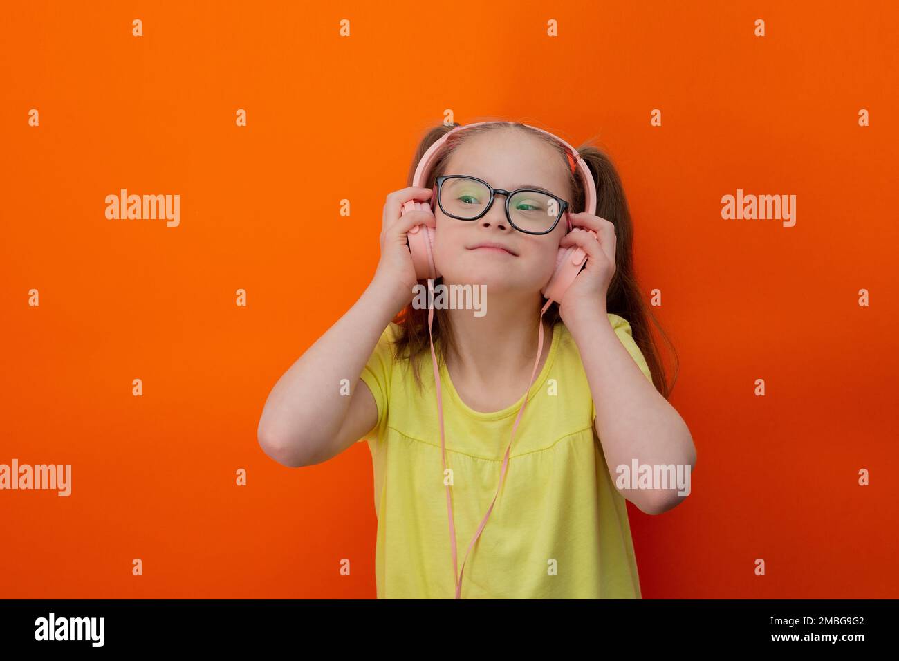 Girl with Down syndrome listens to music. Orange background Stock Photo