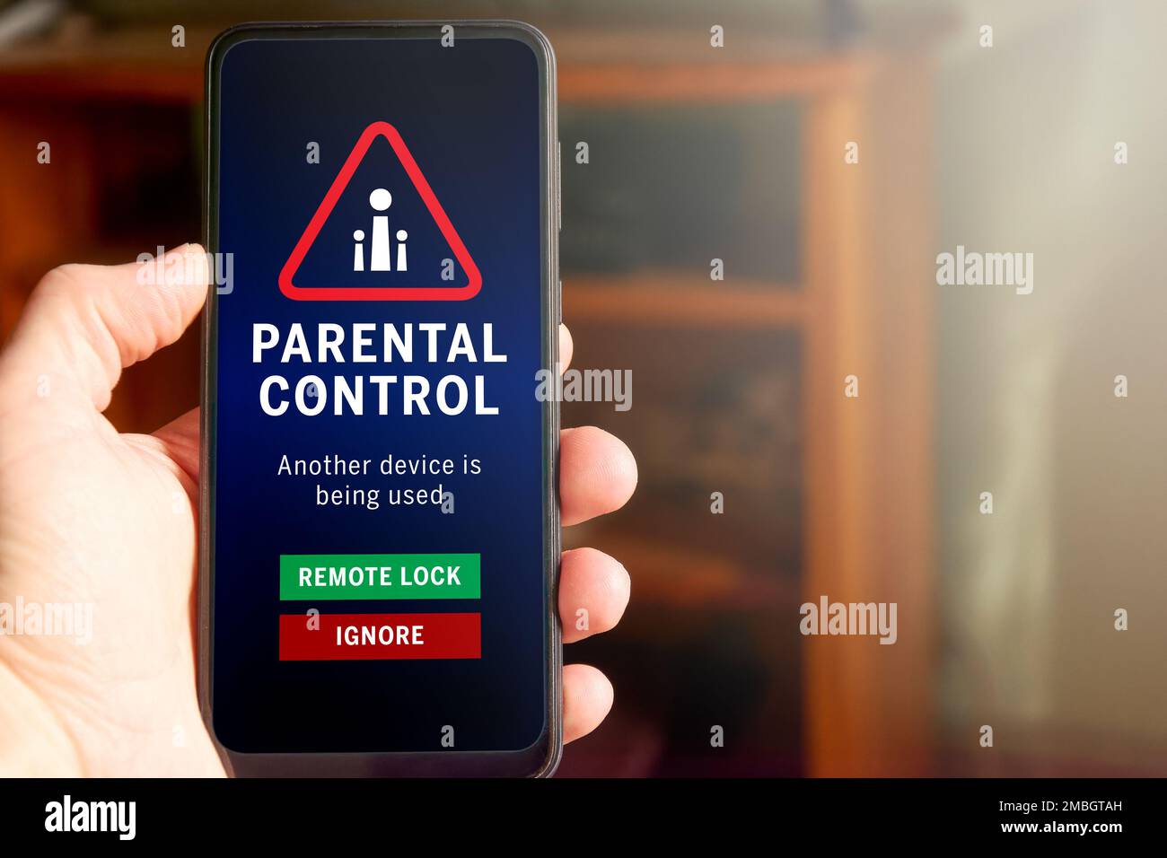 Male hand holding mobile phone with parental control warning on the screen: 'Another device is being used'. Buttons with options to remote lock or ign Stock Photo