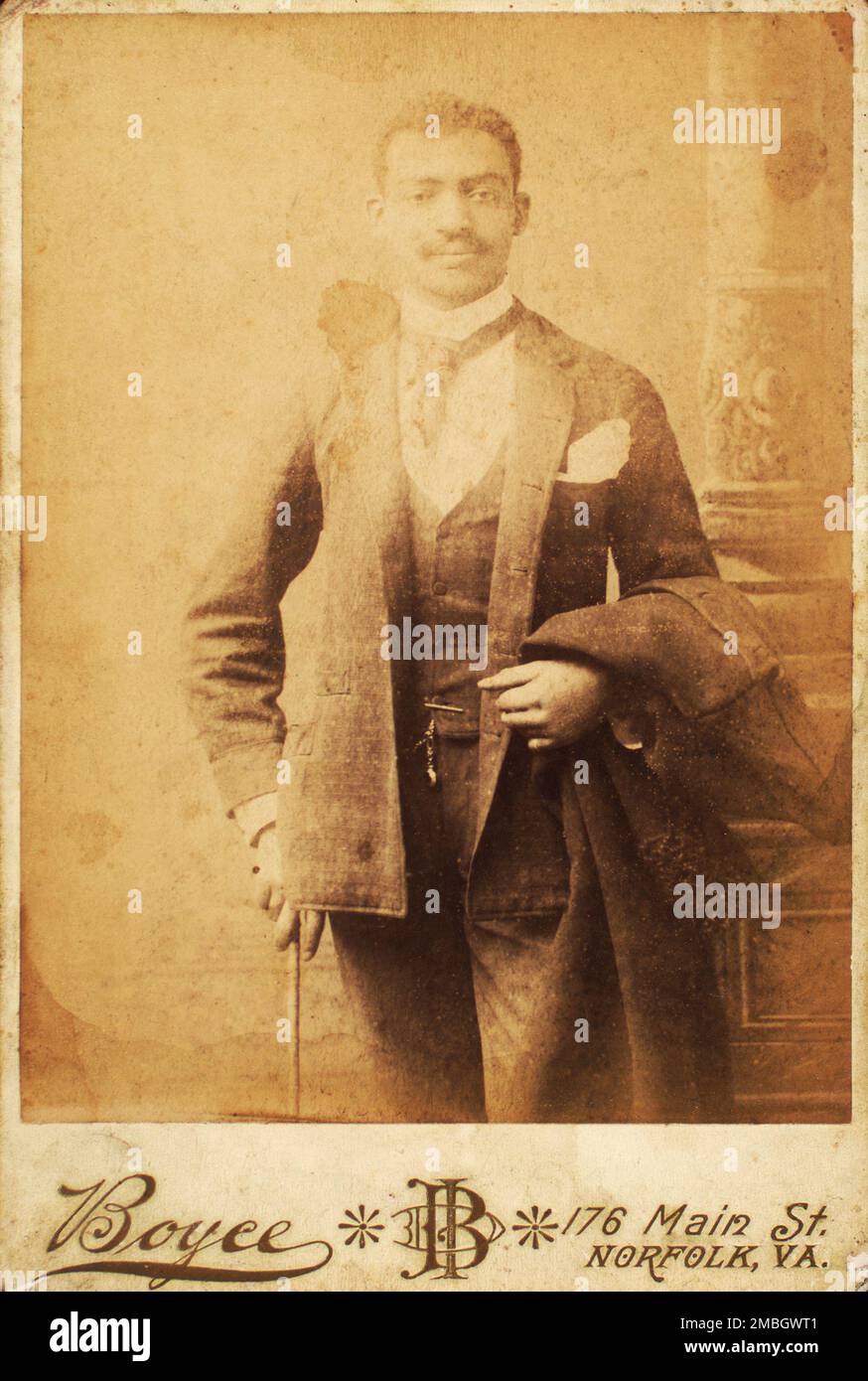 Dapper man, coat draped over his arm, and cane in hand, c1880-c1889. Stock Photo