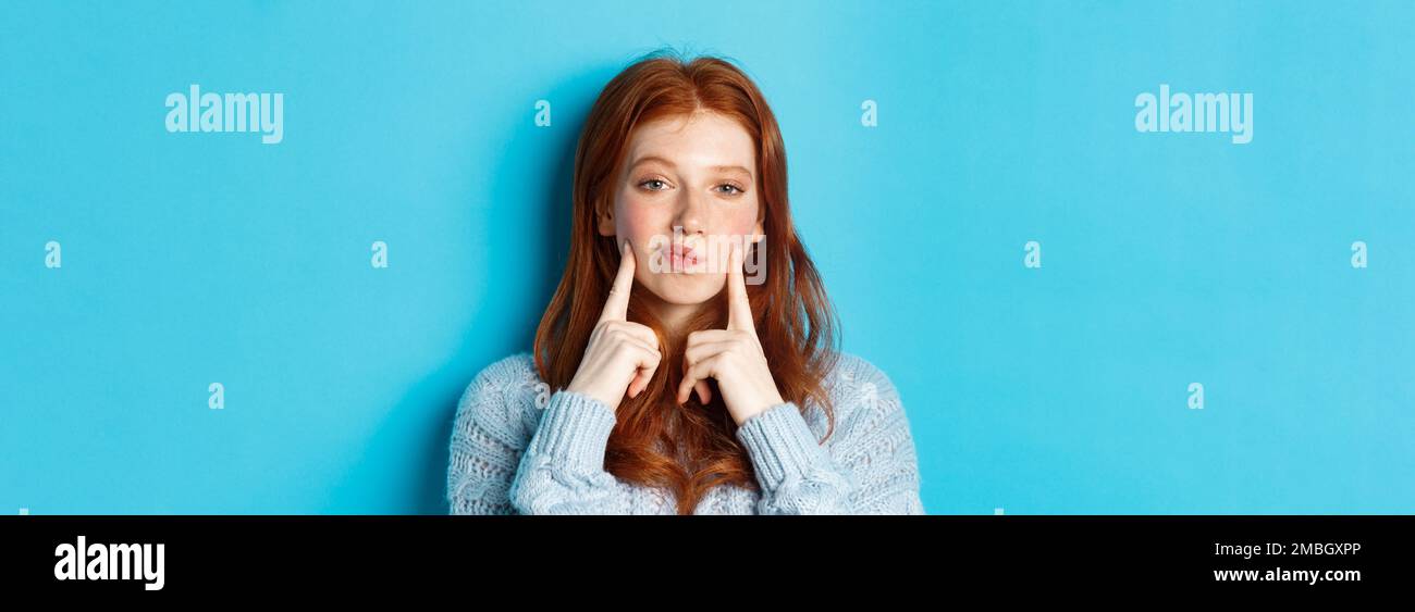 Close-up of cute redhead girl in sweater, pucker lips and pointing ...