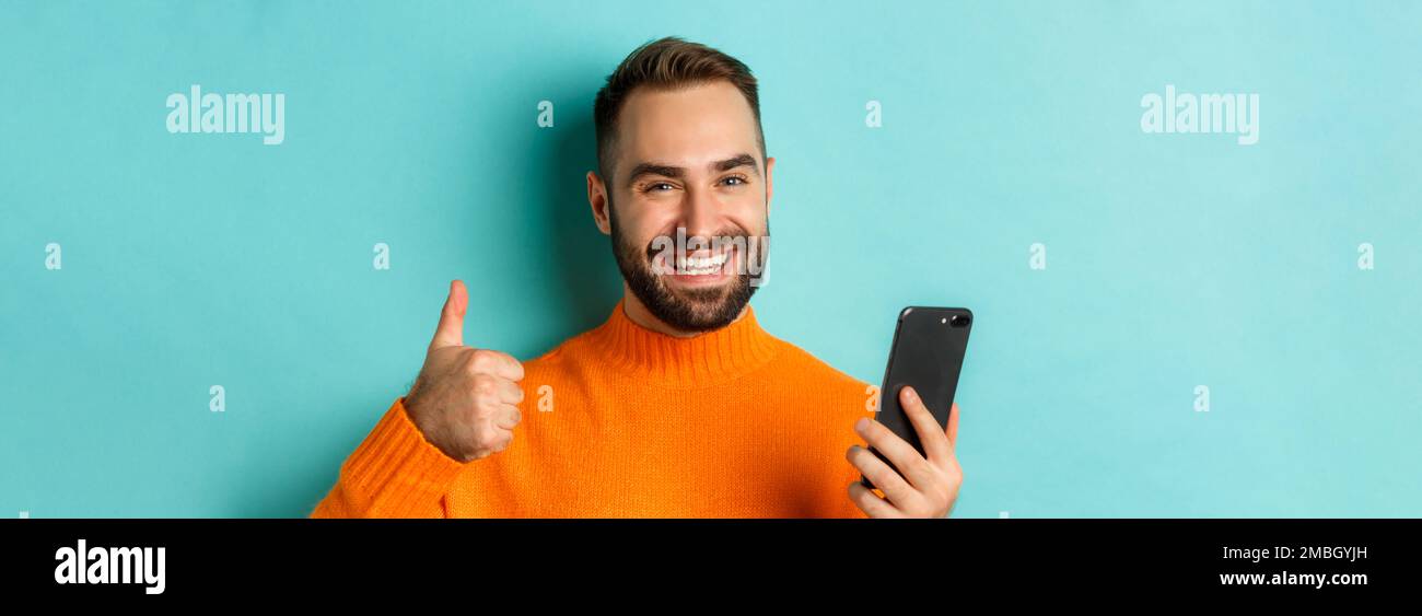 Close-up of bearded man holding smartphone, thumbs up, recommending ...