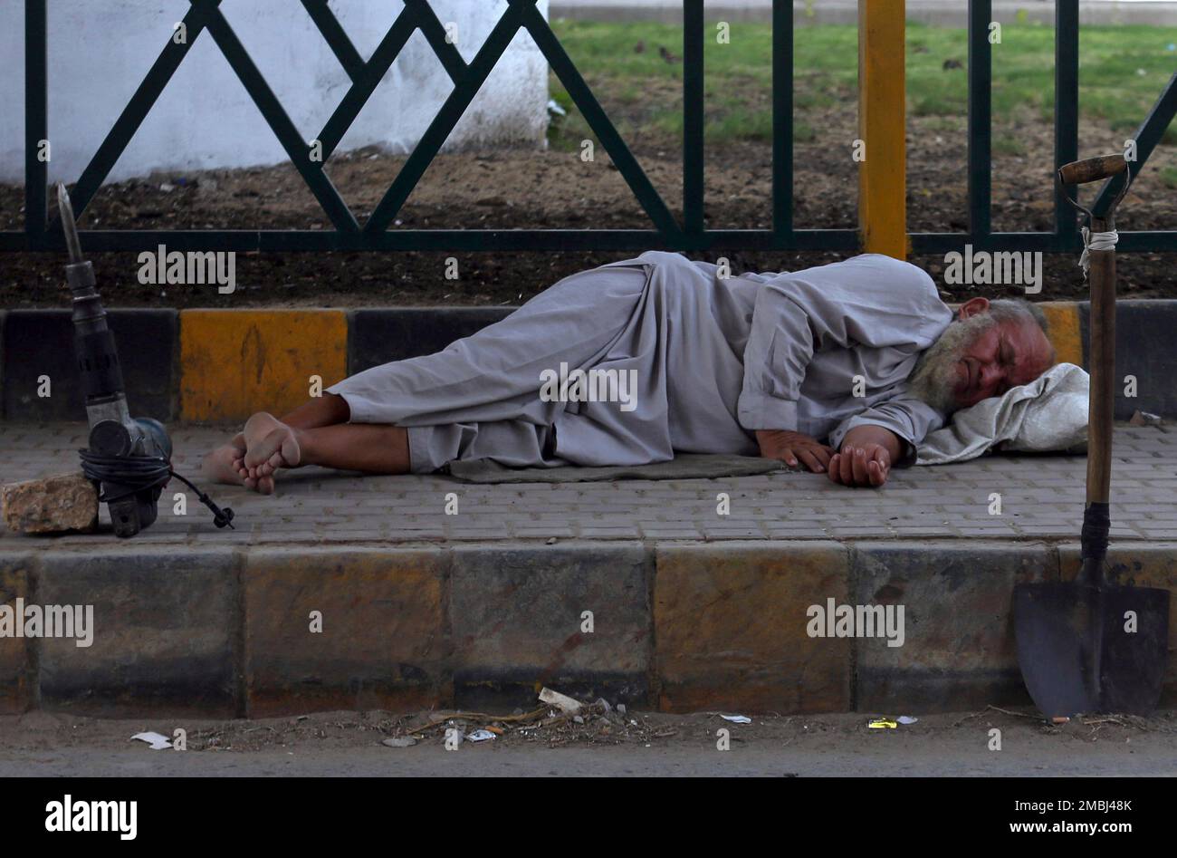 A Pakistani day laborer naps next to his tools as he waits for work on