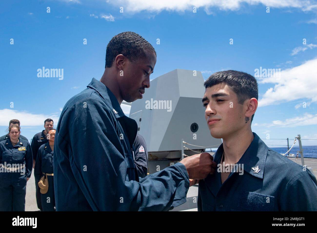 PHILIPPINE SEA (June 16, 2022) Gunner’s Mate 3rd Class Joel Ramirez, right, from Modesto, Calif., receives his petty officer 3rd class collar device on the forecastle of the Arleigh Burke-class guided-missile destroyer USS Spruance (DDG 111). Abraham Lincoln Strike Group is on a scheduled deployment in the U.S. 7th Fleet area of operations to enhance interoperability through alliances and partnerships while serving as a ready-response force in support of a free and open Indo-Pacific region. Stock Photo