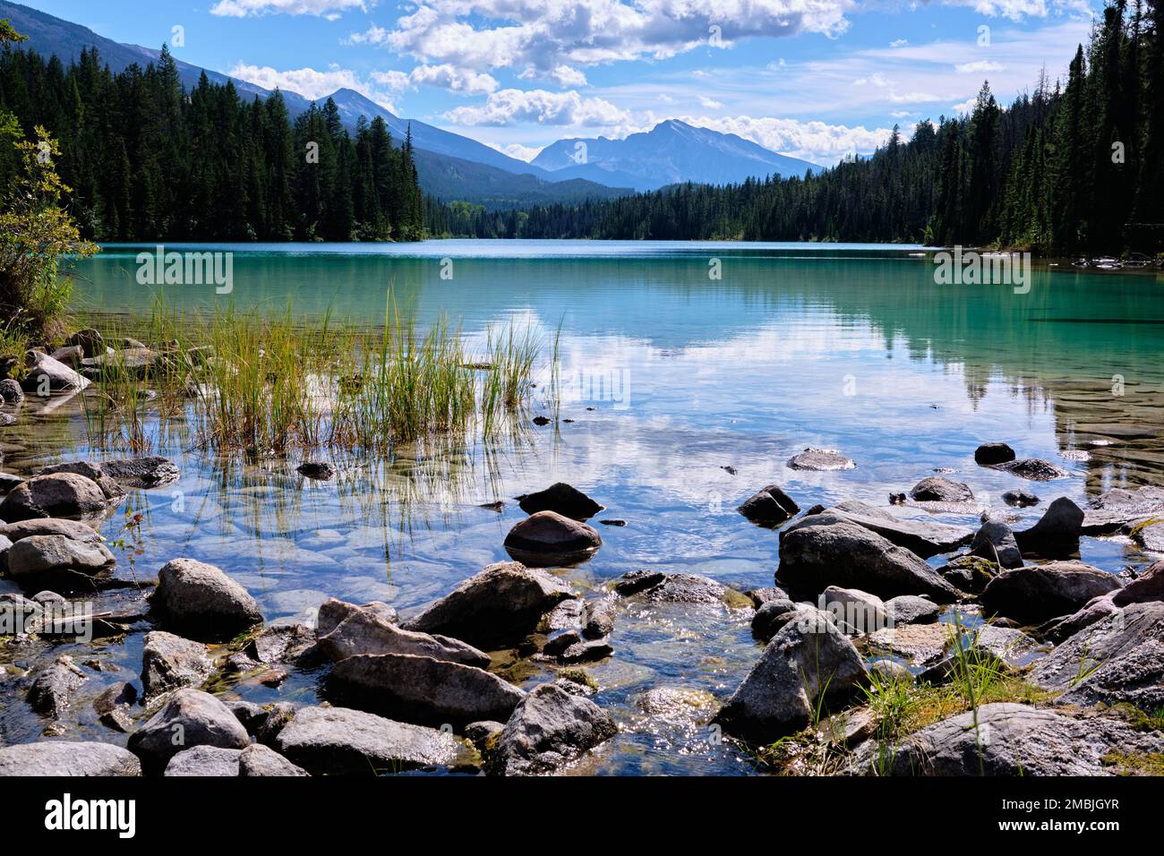 Looking south along Lake One of Valley of the Five Lakes trail in Jasper National Park.  Rocks and grasses in foreground lead into lake and scenery. Stock Photo