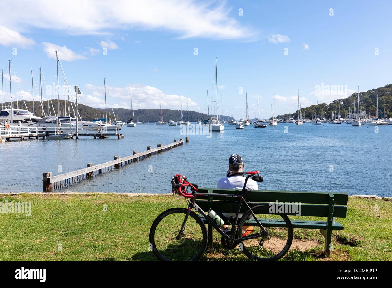 Male road cyclist takes a break Bayview Sydney Australia on park bench enjoying the views across Pittwater and boat marina summer 2023 Stock Photo