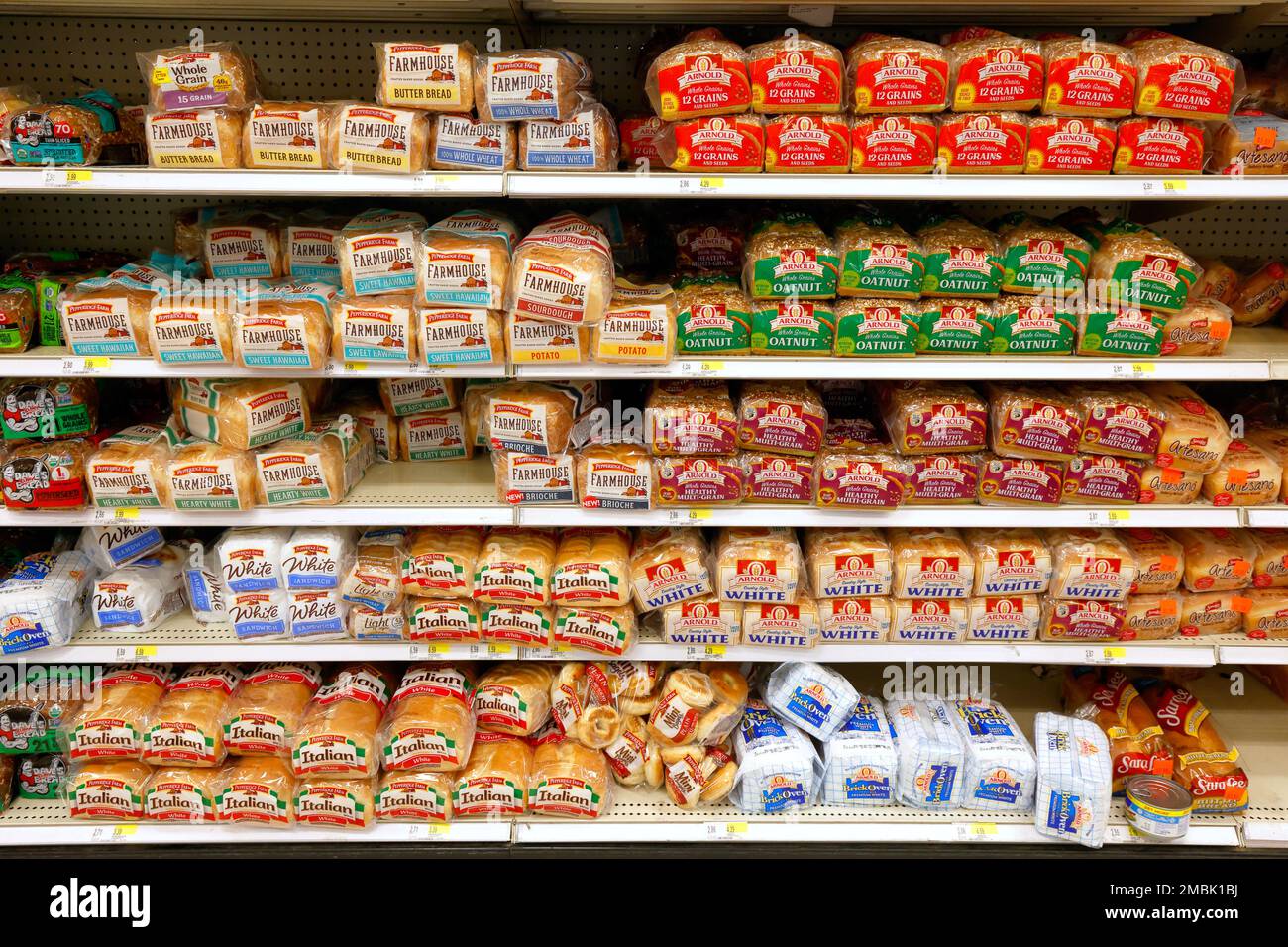 Different varieties of mass produced white bread on an American supermarket grocery store shelf. Stock Photo