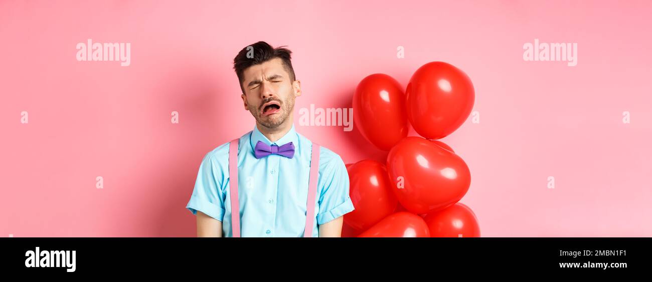 Valentines concept. Sad and heartbroken man crying over break-up, being cheated on lovers day, sobbing and feeling lonely, standing on pink background Stock Photo